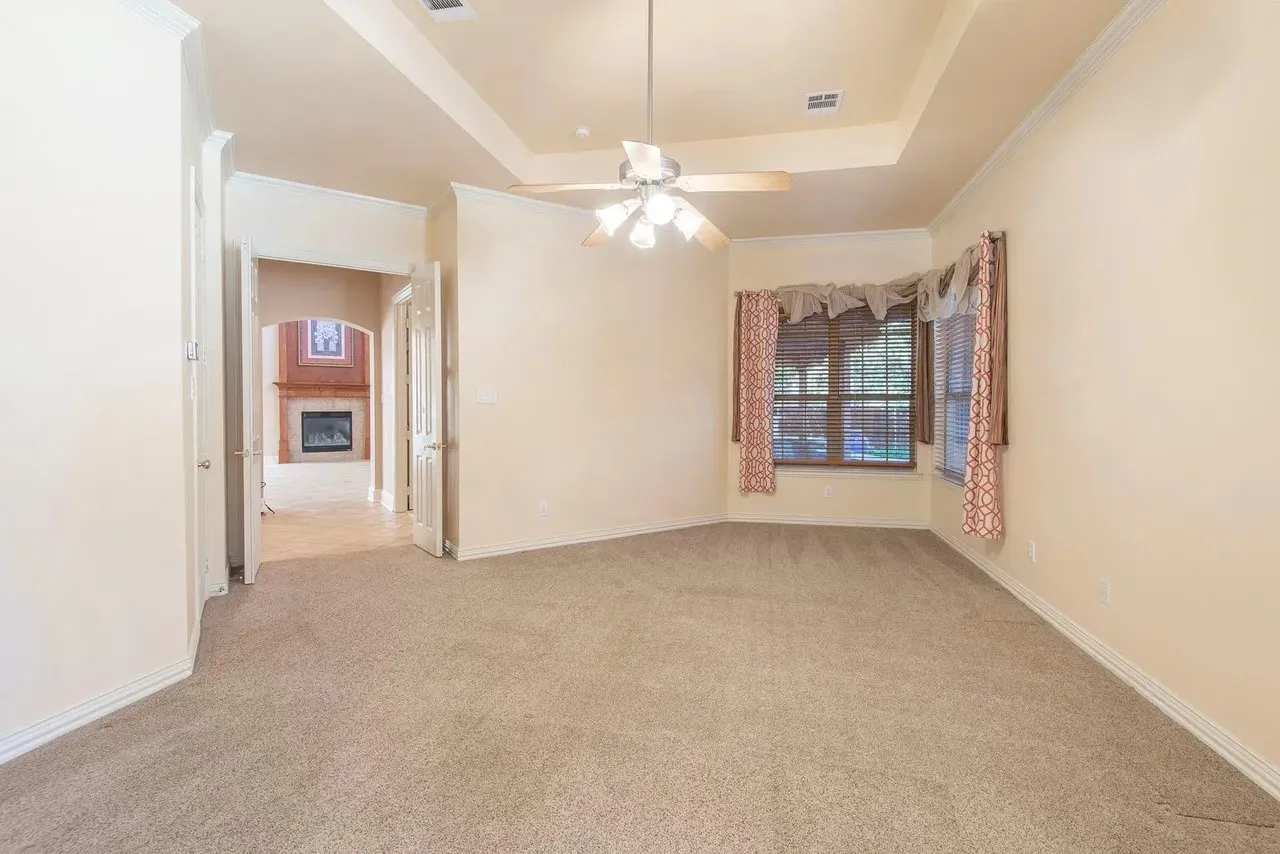 Carpeted room featuring a ceiling fan, tray ceiling, bay window, and arched doorway