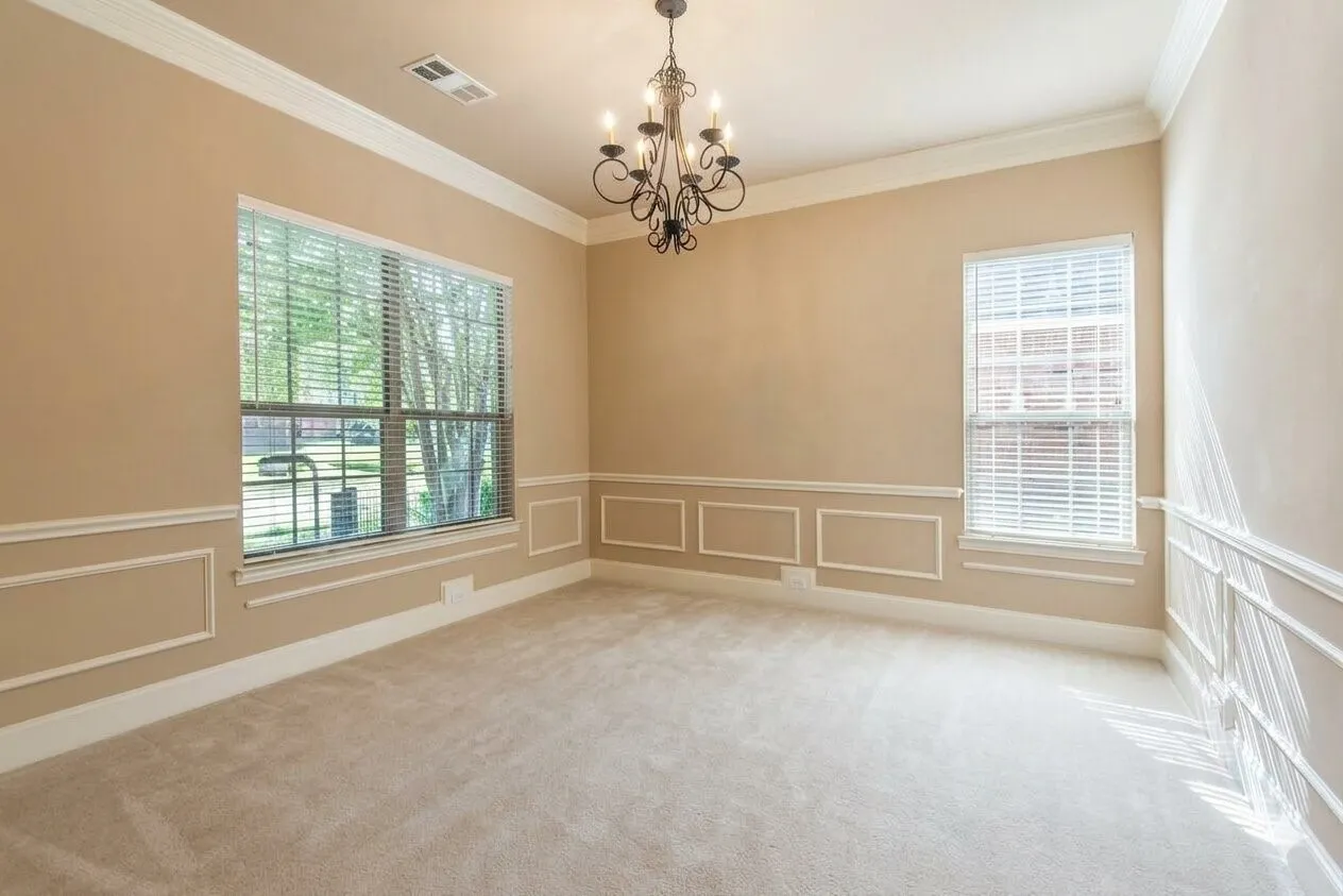 Spacious room featuring neutral carpeting, decorative wainscoting, crown molding, and an ornate wrought-iron chandelier