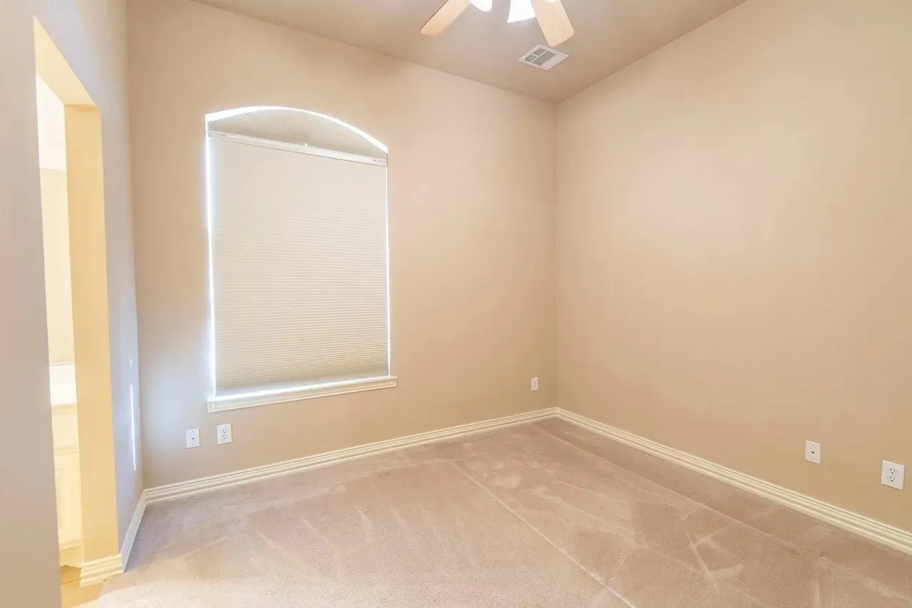 Room featuring a wide arched window with a roller shade, light neutral wall paint, carpet flooring, a ceiling fan, and white baseboards