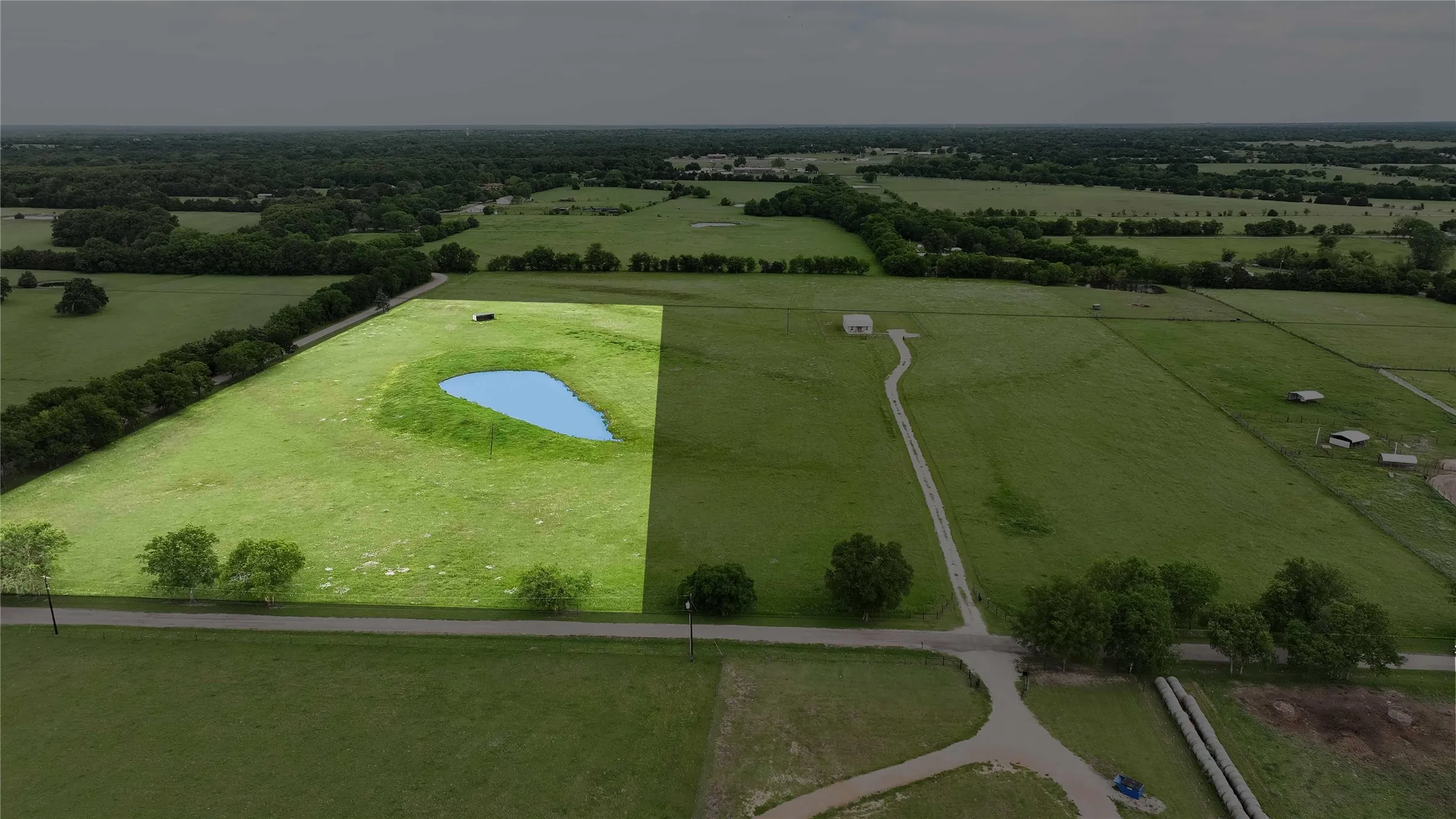 Expansive green acreage featuring a visible pond and perimeter tree line