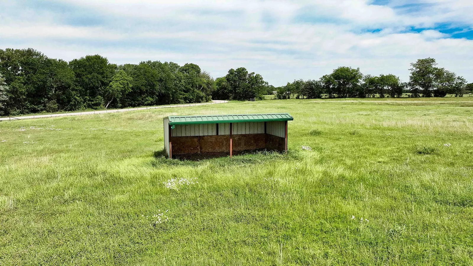 Agricultural outbuilding with a green metal roof, set within a vast grassy expanse