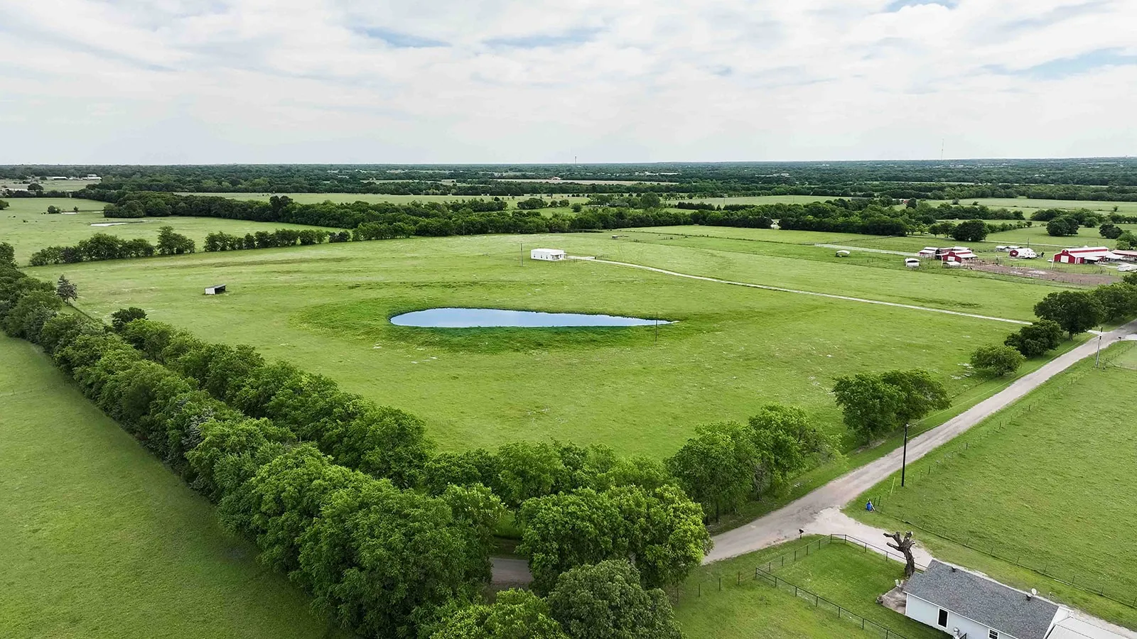 Expansive green pastures featuring a prominent pond and mature tree lines