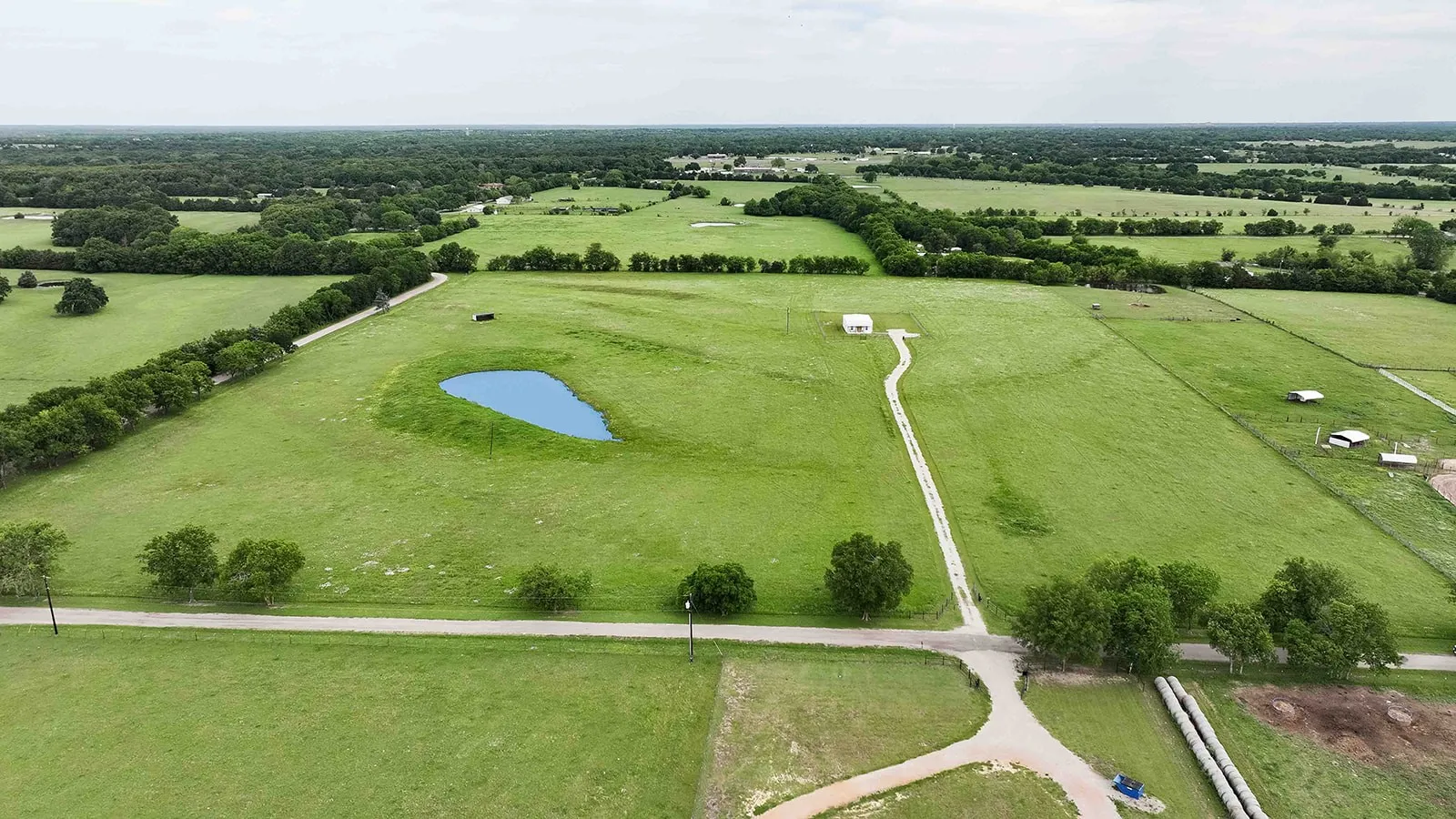Expansive green acreage featuring a private pond, a white structure, and a long gravel driveway