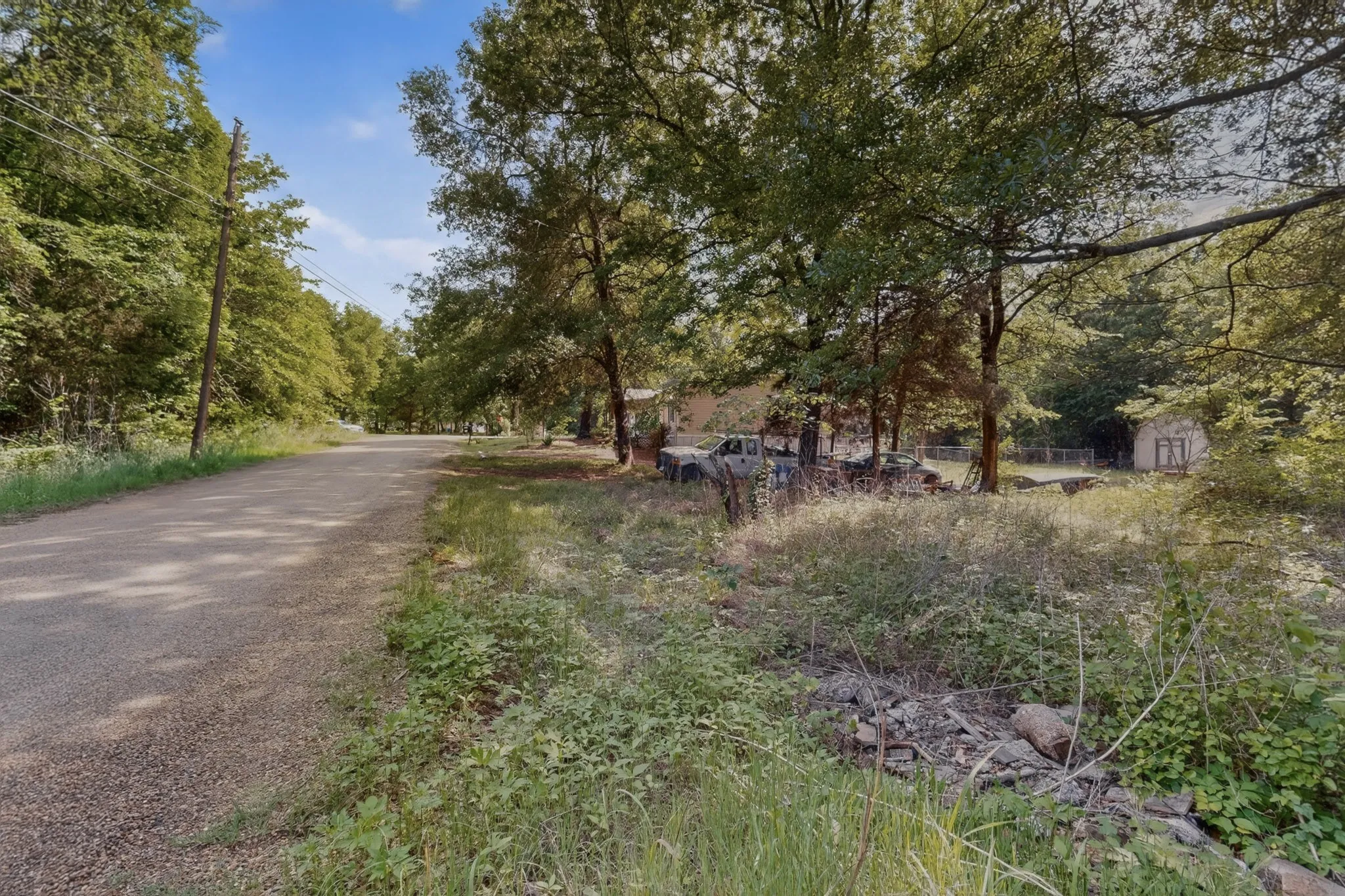 Expansive wooded lot with a gravel road frontage and a visible storage shed