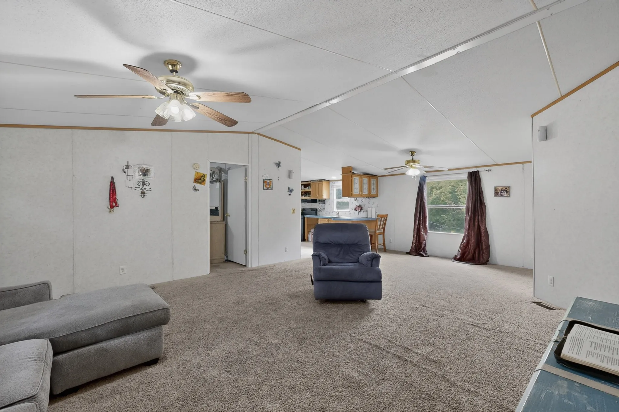 Spacious open concept living area featuring carpet flooring, white walls, and a ceiling fan with light fixture
