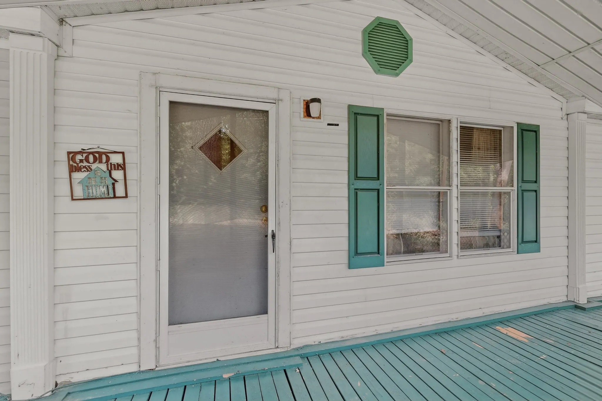 The property features white siding, a front entry door with a decorative glass insert, and windows with green shutters