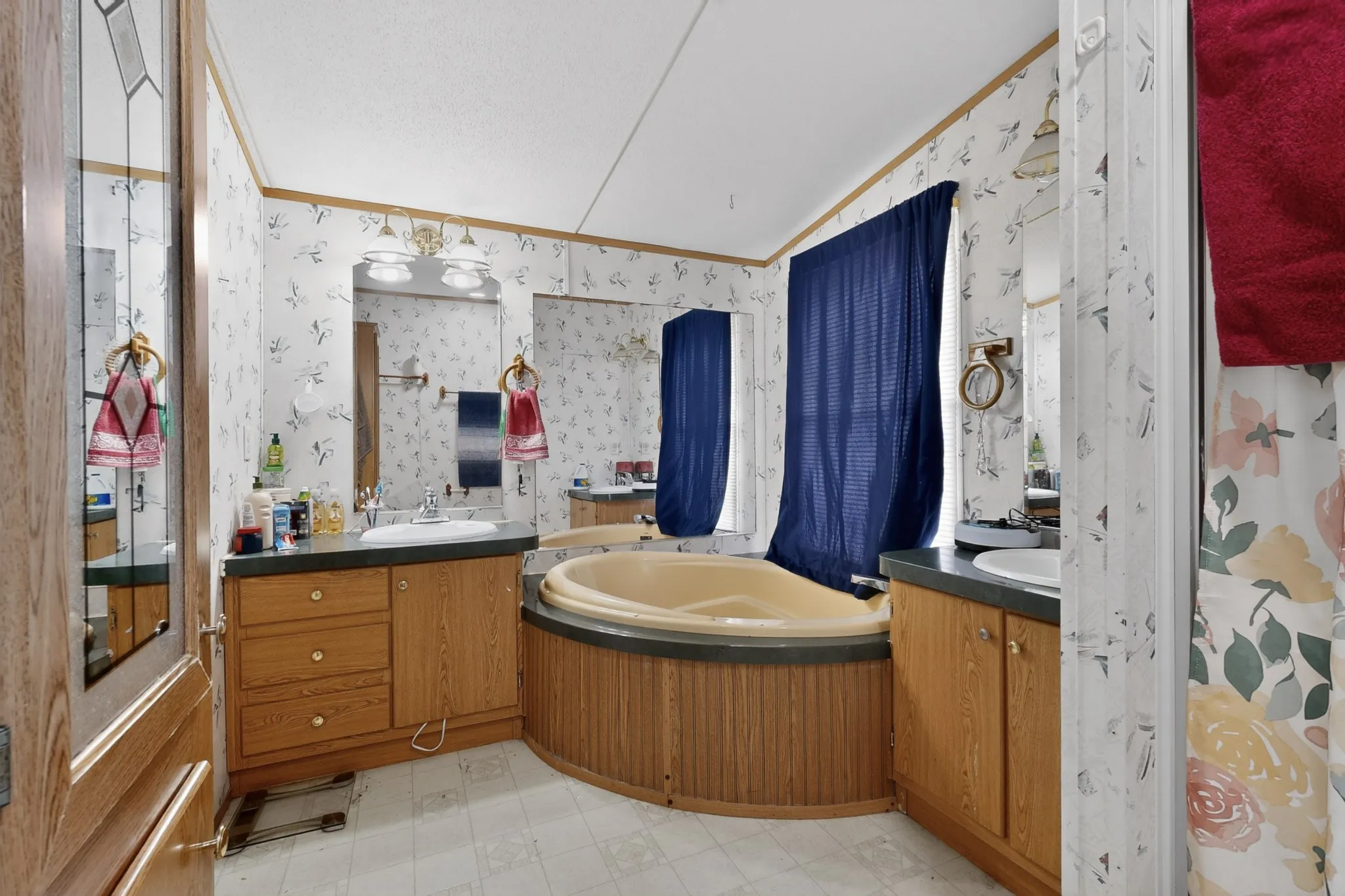 The bathroom features a corner soaking tub, a vanity with a white basin and ample cabinet storage, and a mirrored wall with an overhead light fixture
