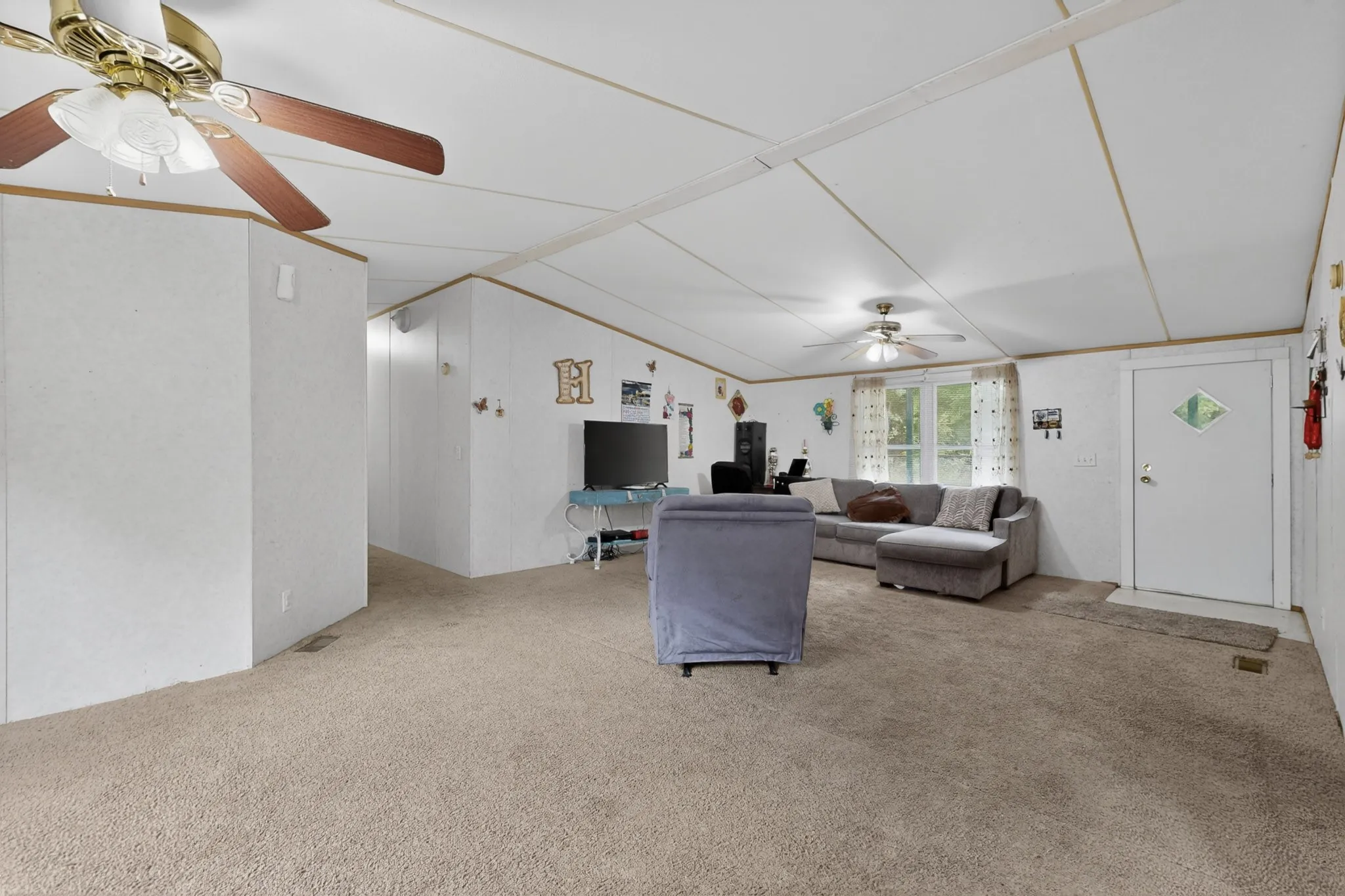 Spacious living area featuring neutral carpeting, white walls, and a ceiling fan