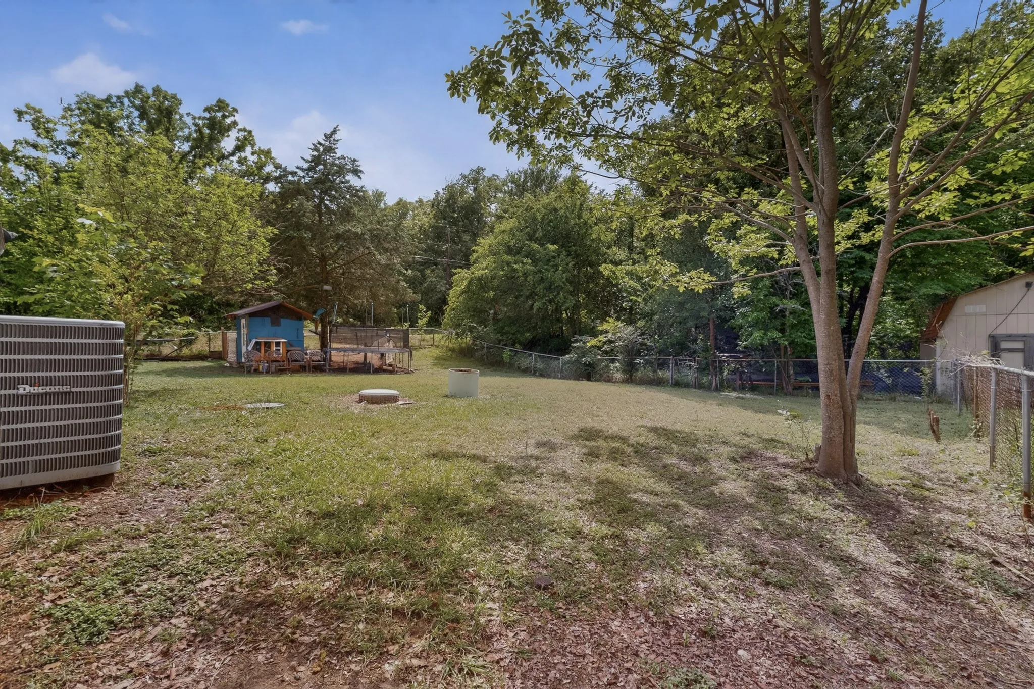 The property features an expansive yard with a lawn, mature trees, and a utility shed with a fenced area