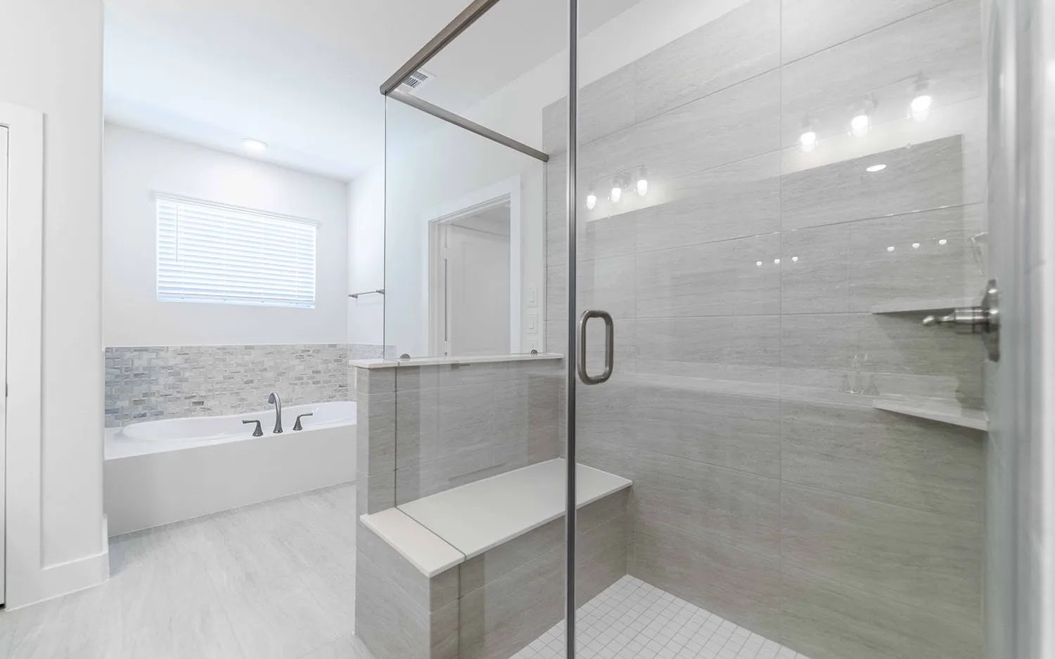 Spacious bathroom featuring a frameless glass shower enclosure with a built-in bench, a separate soaking tub with a mosaic tile surround, and light-toned tile flooring