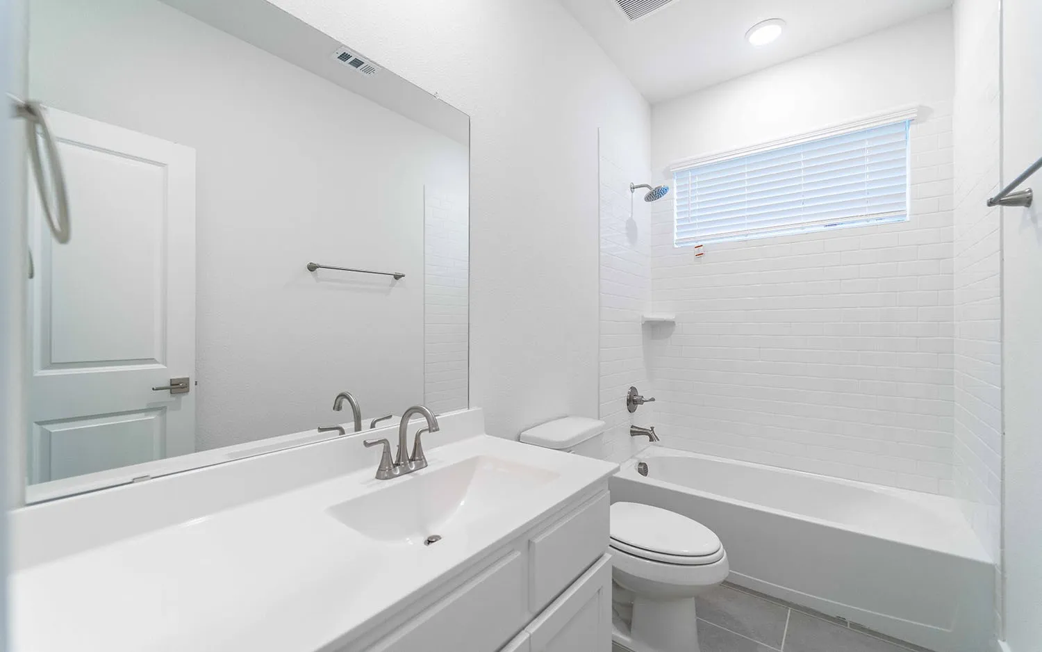 Bright bathroom featuring a single vanity with integrated sink, brushed nickel faucet, and full-width mirror