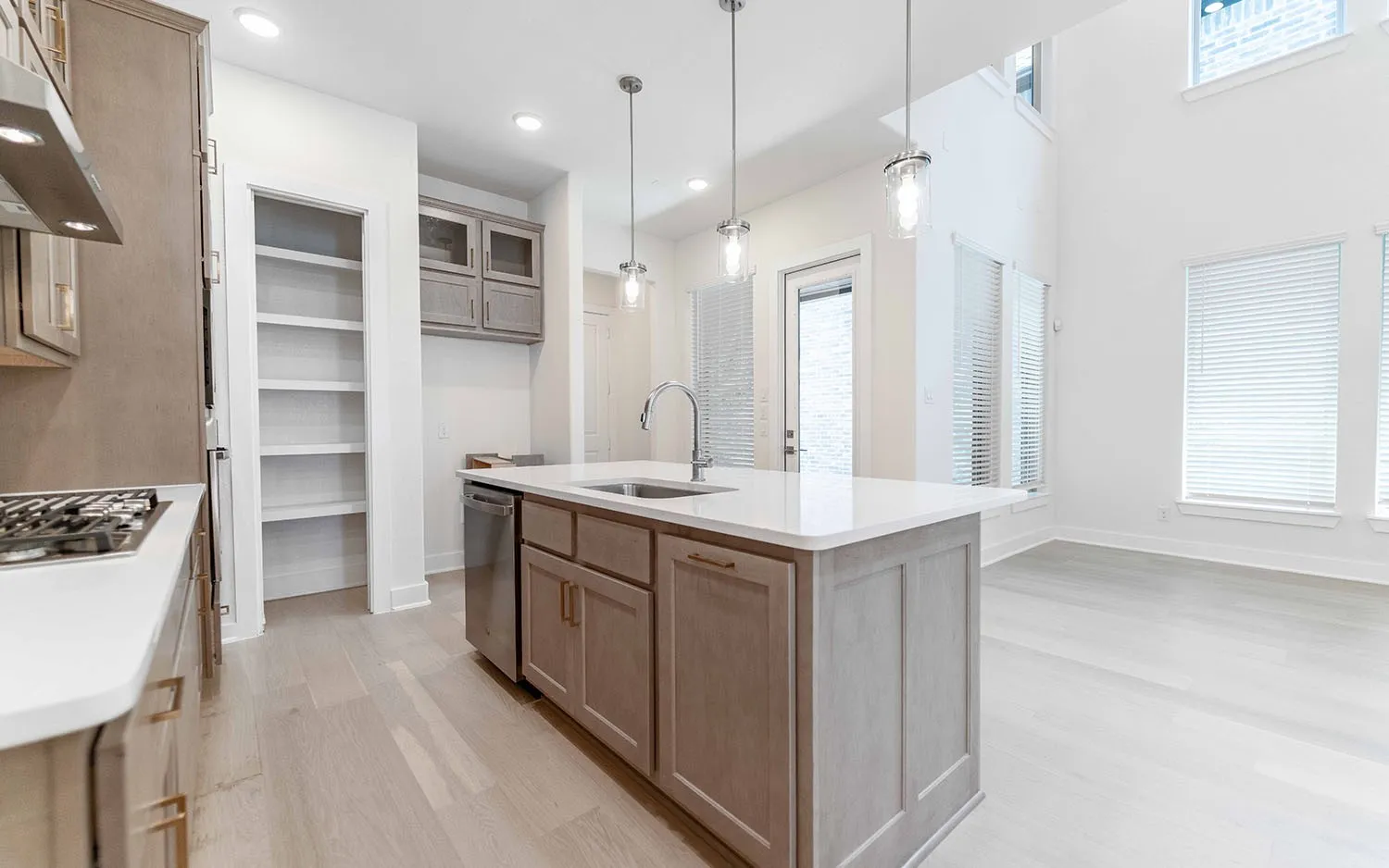 Modern kitchen featuring an island with a stainless steel sink, contemporary pendant lighting, light wood-finish flooring, ample white cabinetry, and a gas cooktop