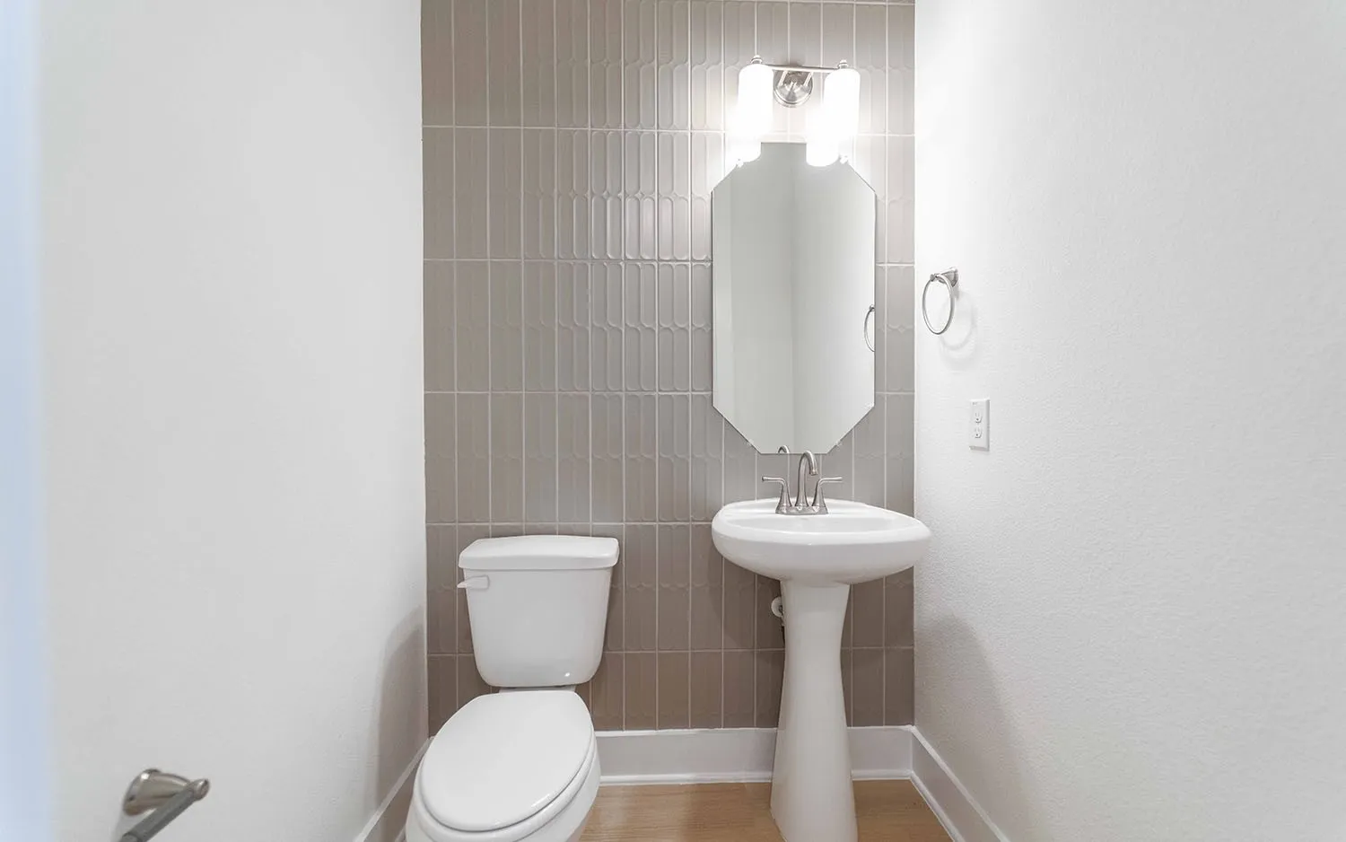 Bathroom featuring a pedestal sink, wall-mounted mirror, and stylish vertical tile accent wall