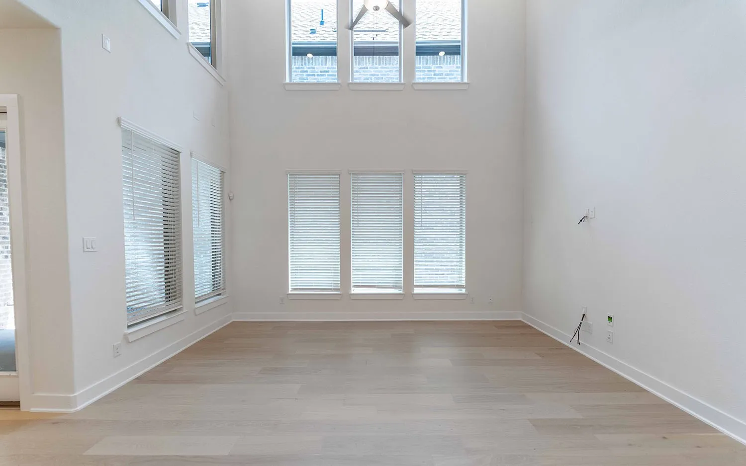 Two-story living area featuring wood-finish flooring, tall ceilings, and multiple windows with blinds