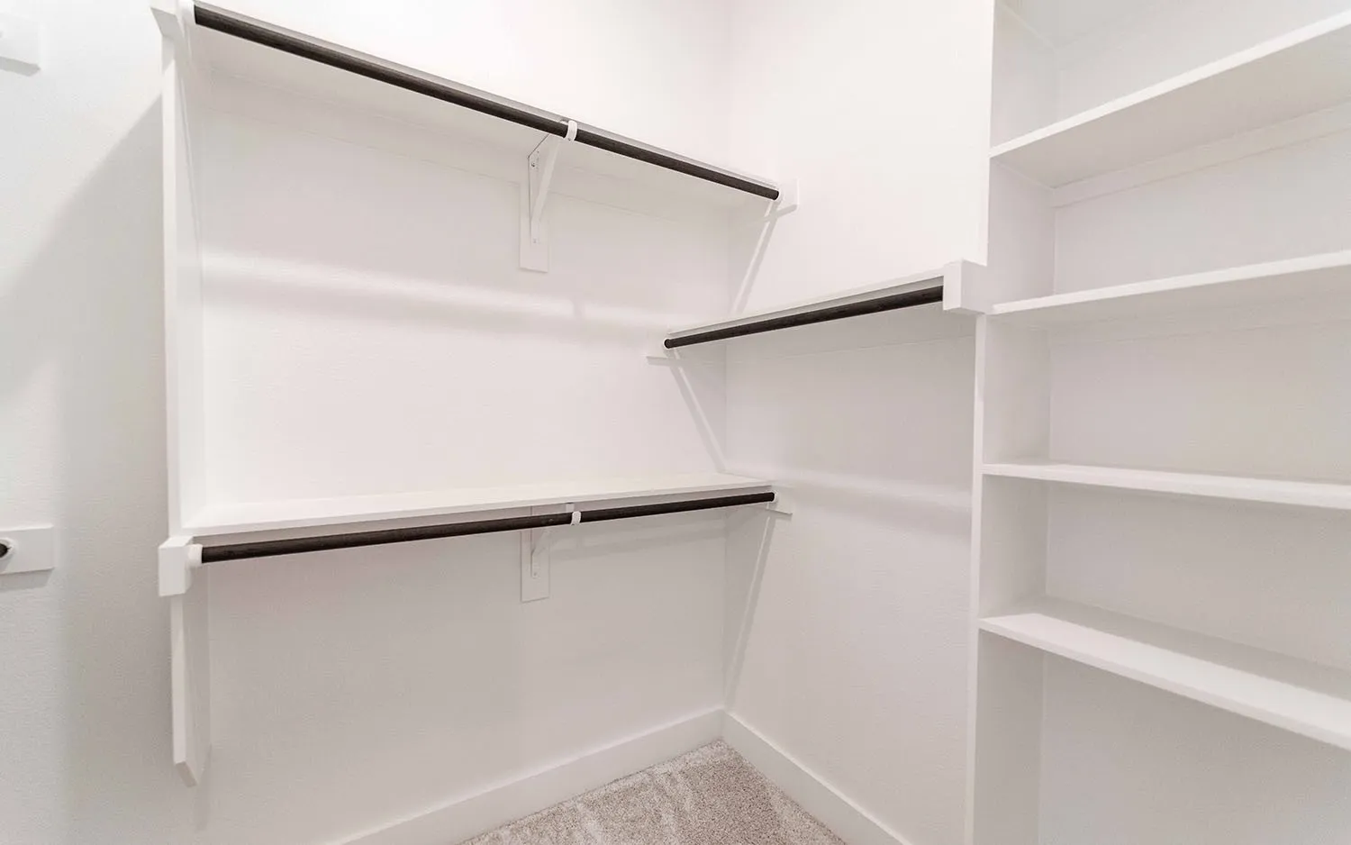 Organized closet featuring multiple white shelving units and dark-finish hanging rods
