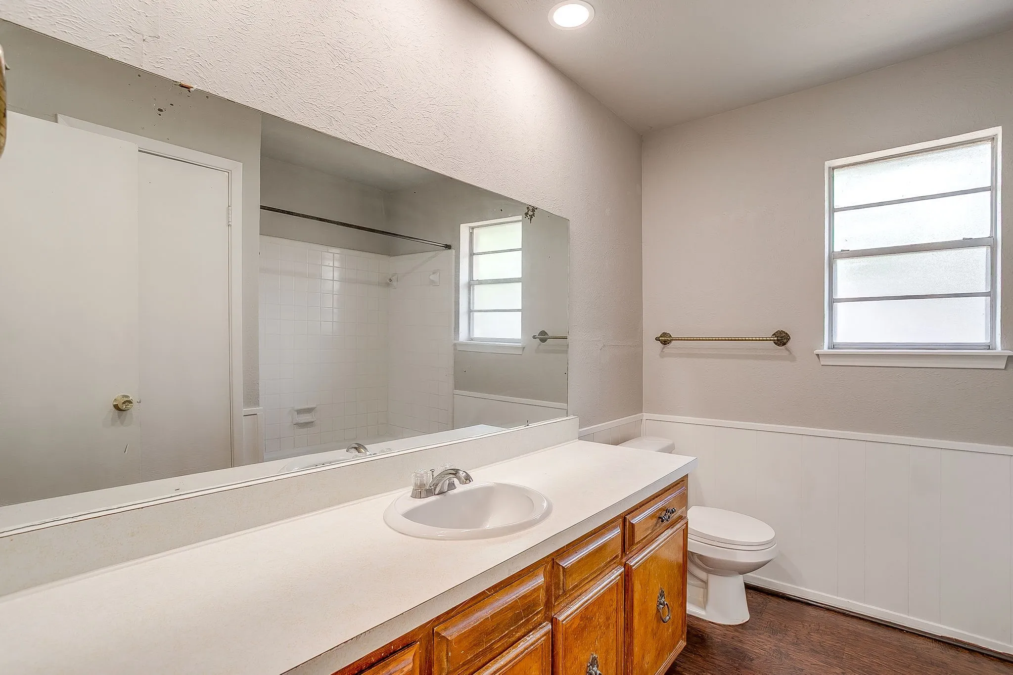 The bathroom features a vanity with a white countertop and wood cabinetry, a white toilet, and a window providing natural light