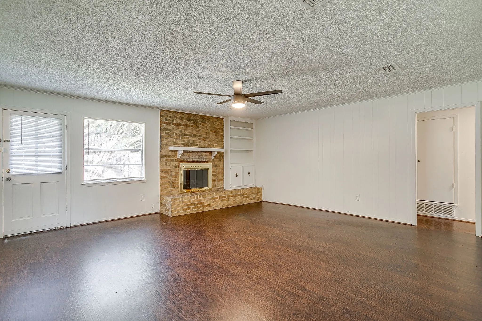 Living area featuring dark wood flooring, a brick fireplace with a mantel, built-in shelving, and a ceiling fan