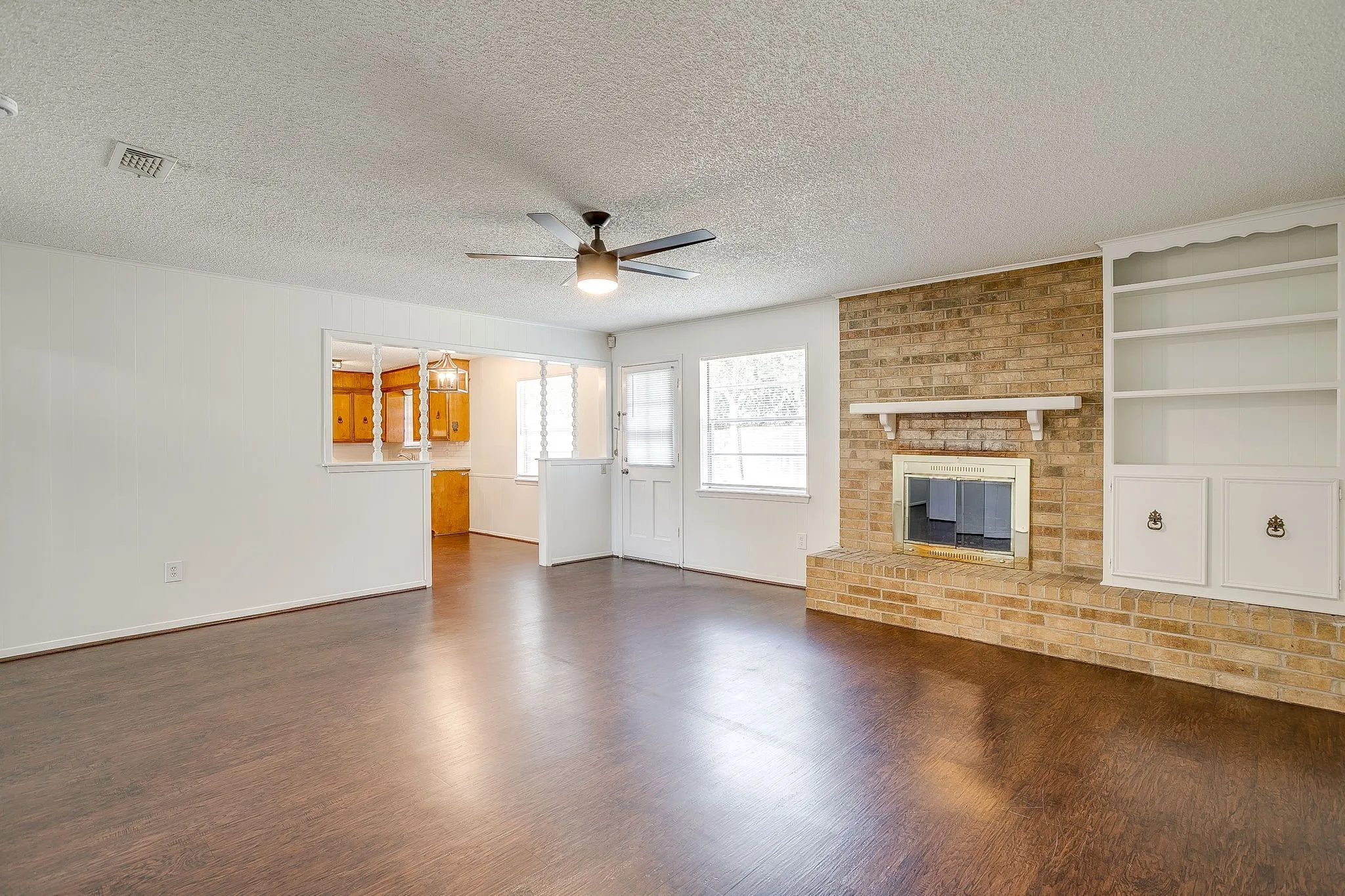 Spacious living area featuring dark wood floors, a brick fireplace, and built-in shelving