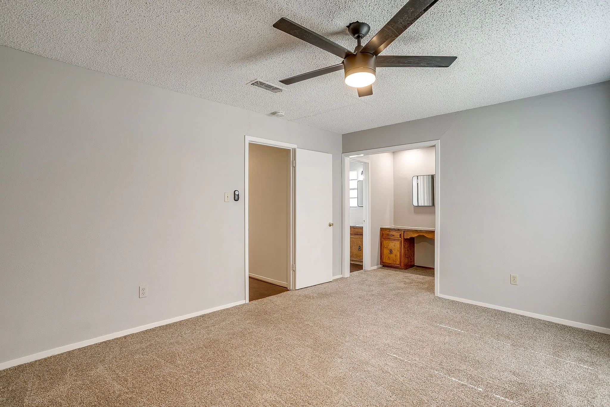 Spacious room featuring light gray walls, carpet flooring, and a ceiling fan with integrated lighting