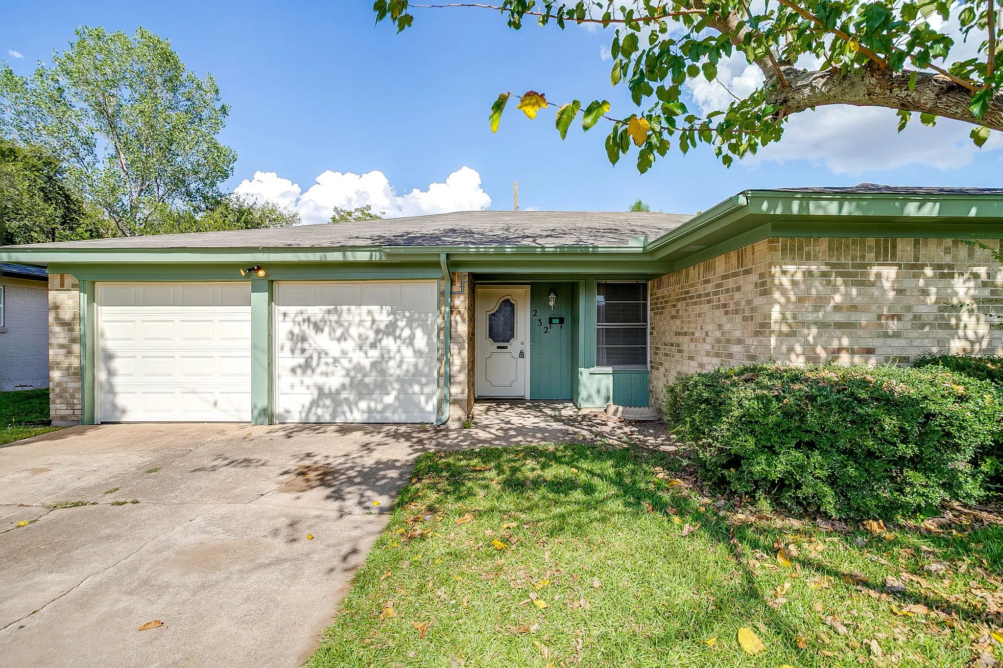 The property features a brick exterior, a two-car garage with white doors, and a front yard with a lawn and mature shrubbery