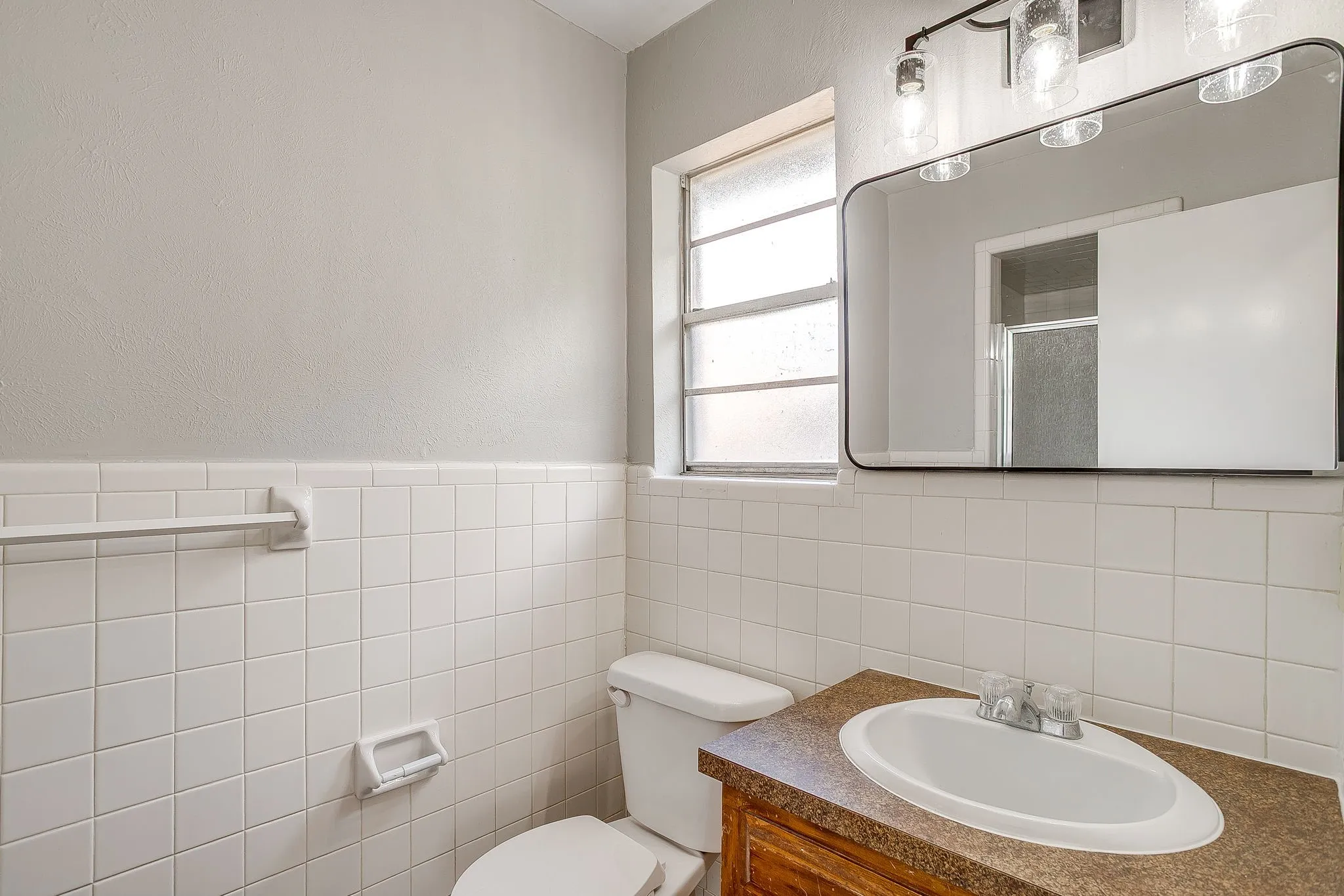 Bathroom featuring a window with frosted glass, a vanity with a sink, and a mirror with overhead lighting