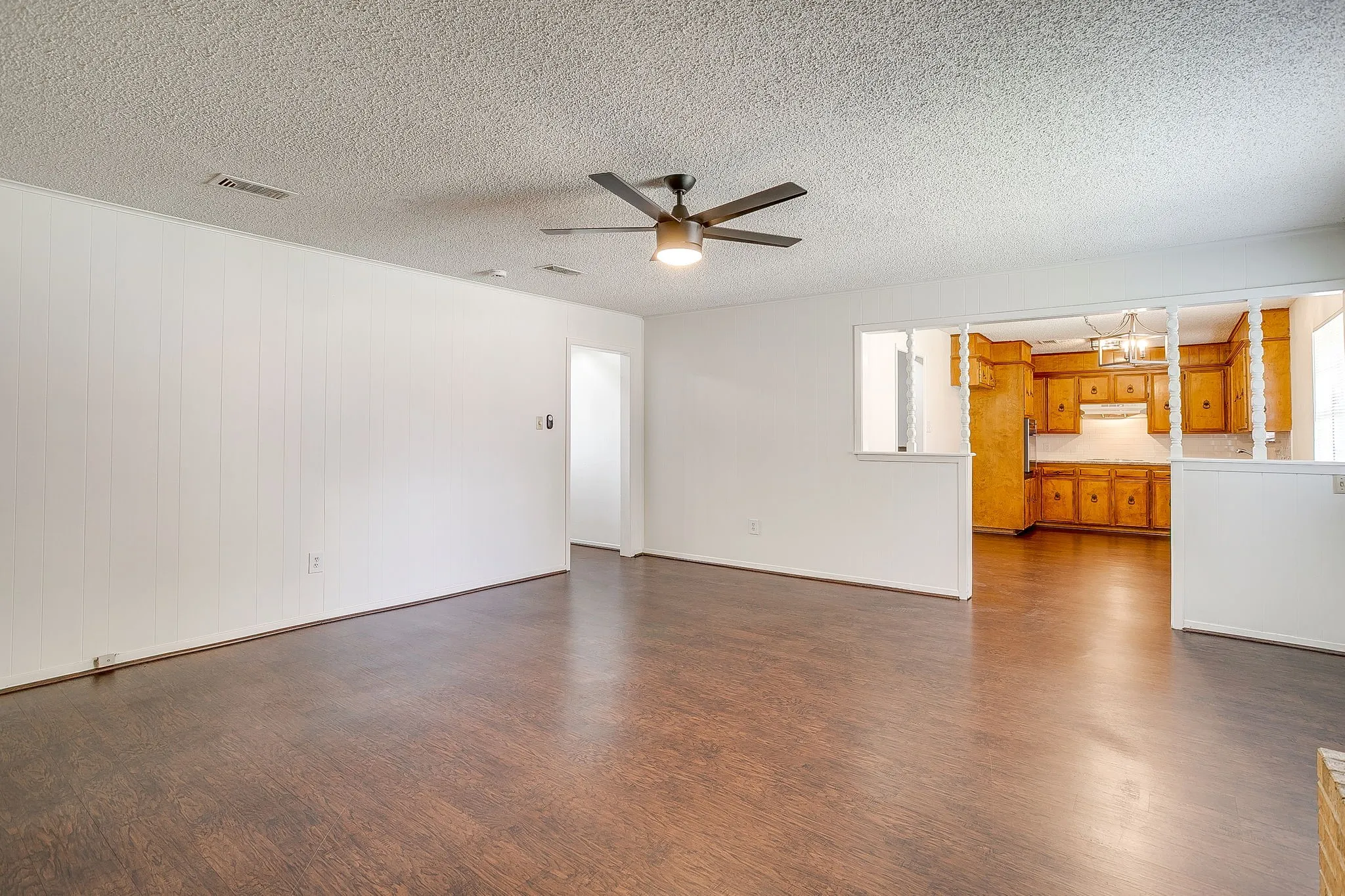 Spacious living area featuring dark wood flooring, white walls, and a ceiling fan with integrated lighting