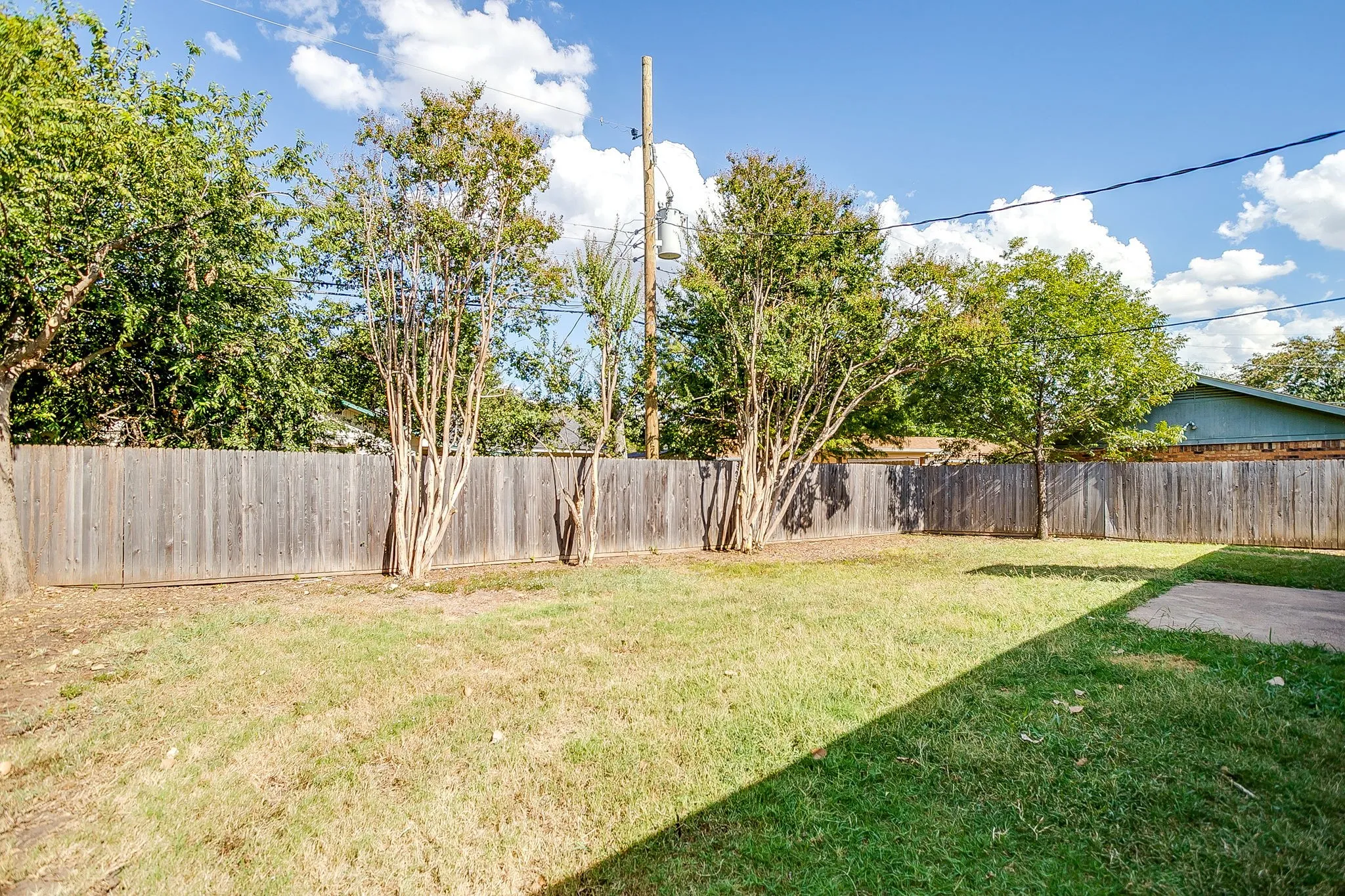 The property features a fenced yard with a lawn and several trees, offering privacy and green space