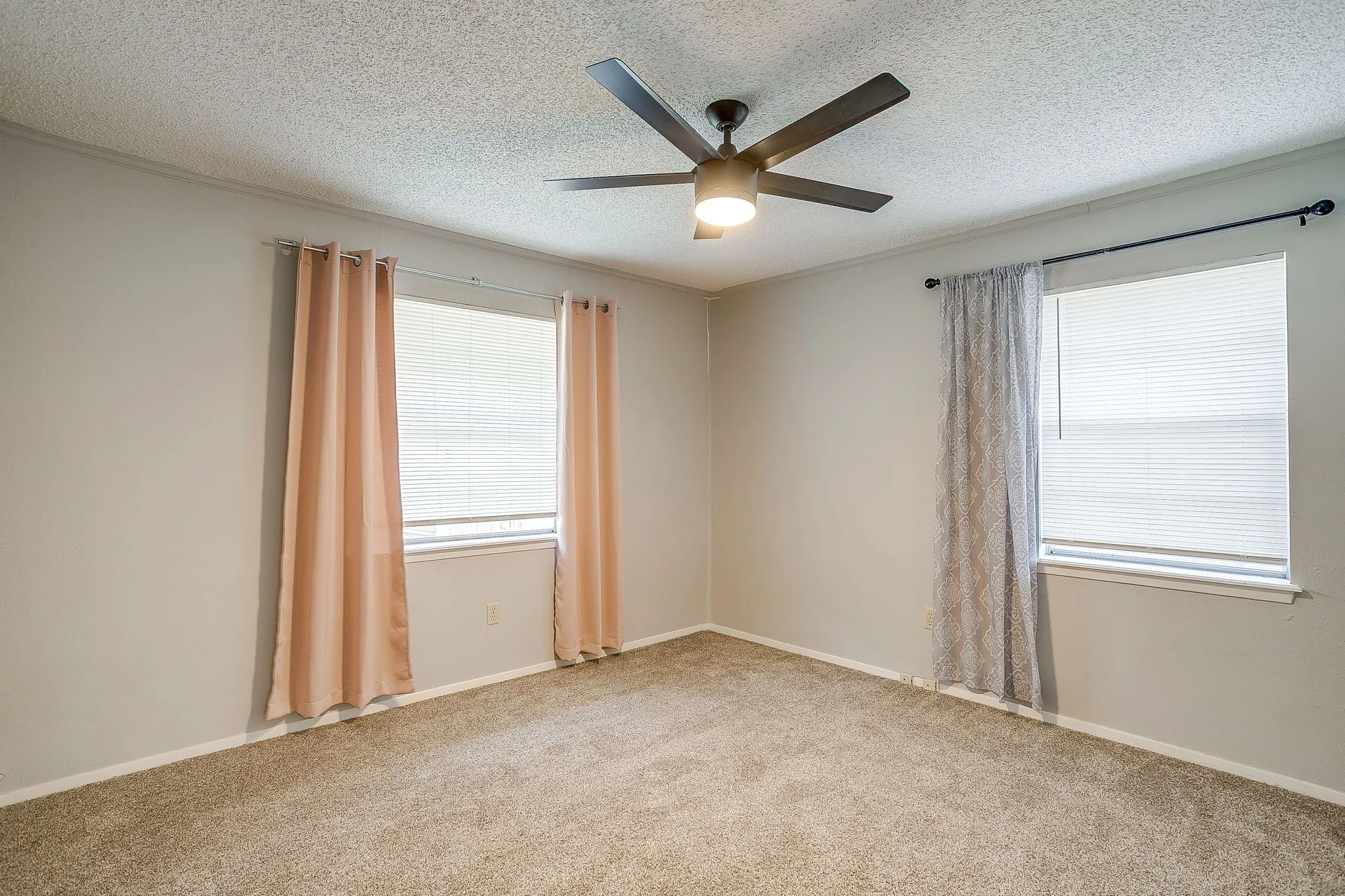 This room features light-colored walls, carpeted flooring, and two windows with blinds and curtains