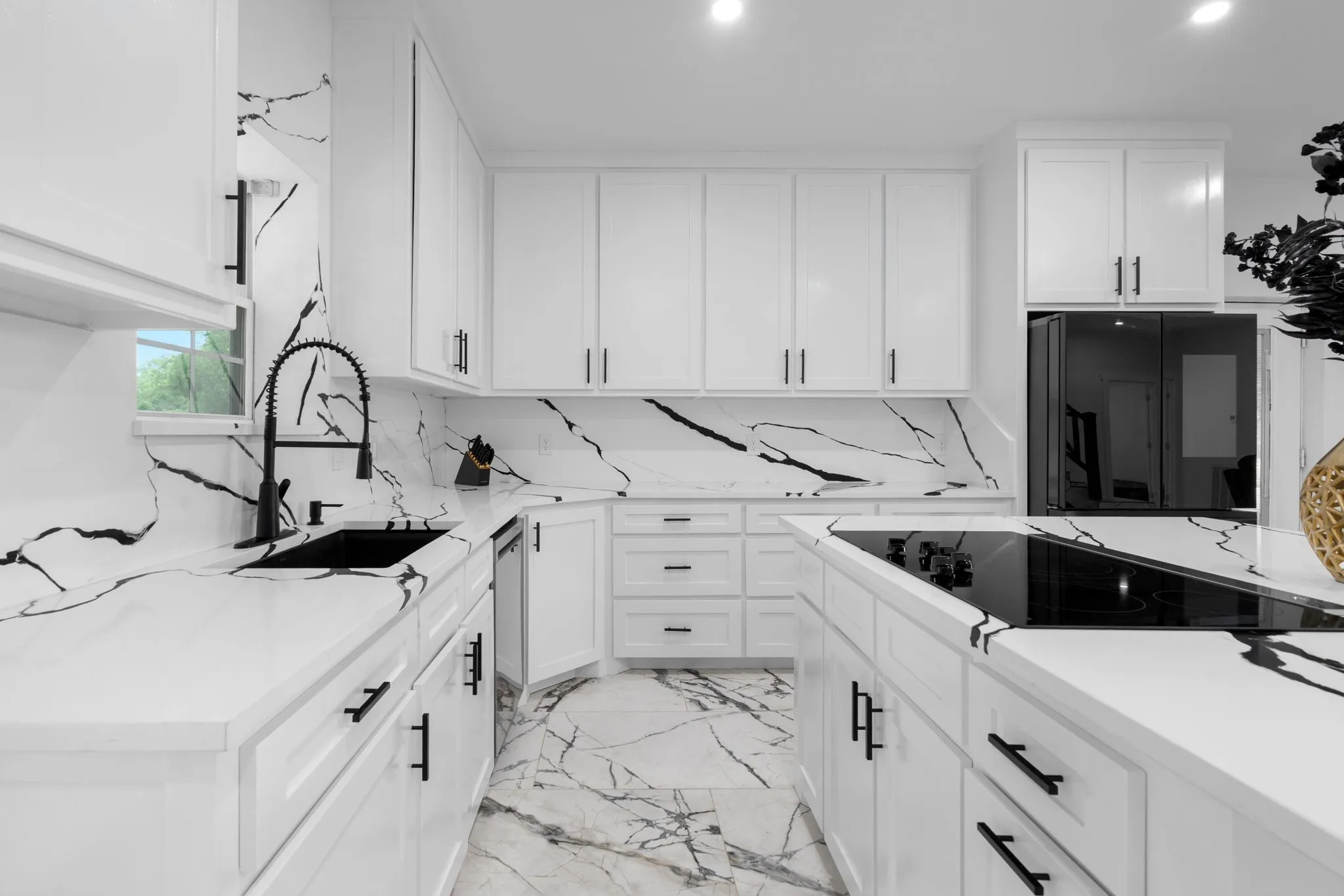 Modern kitchen featuring white cabinetry with matte black hardware, integrated black appliances, a black sink with a gooseneck faucet, quartz countertops, and coordinating quartz backsplash