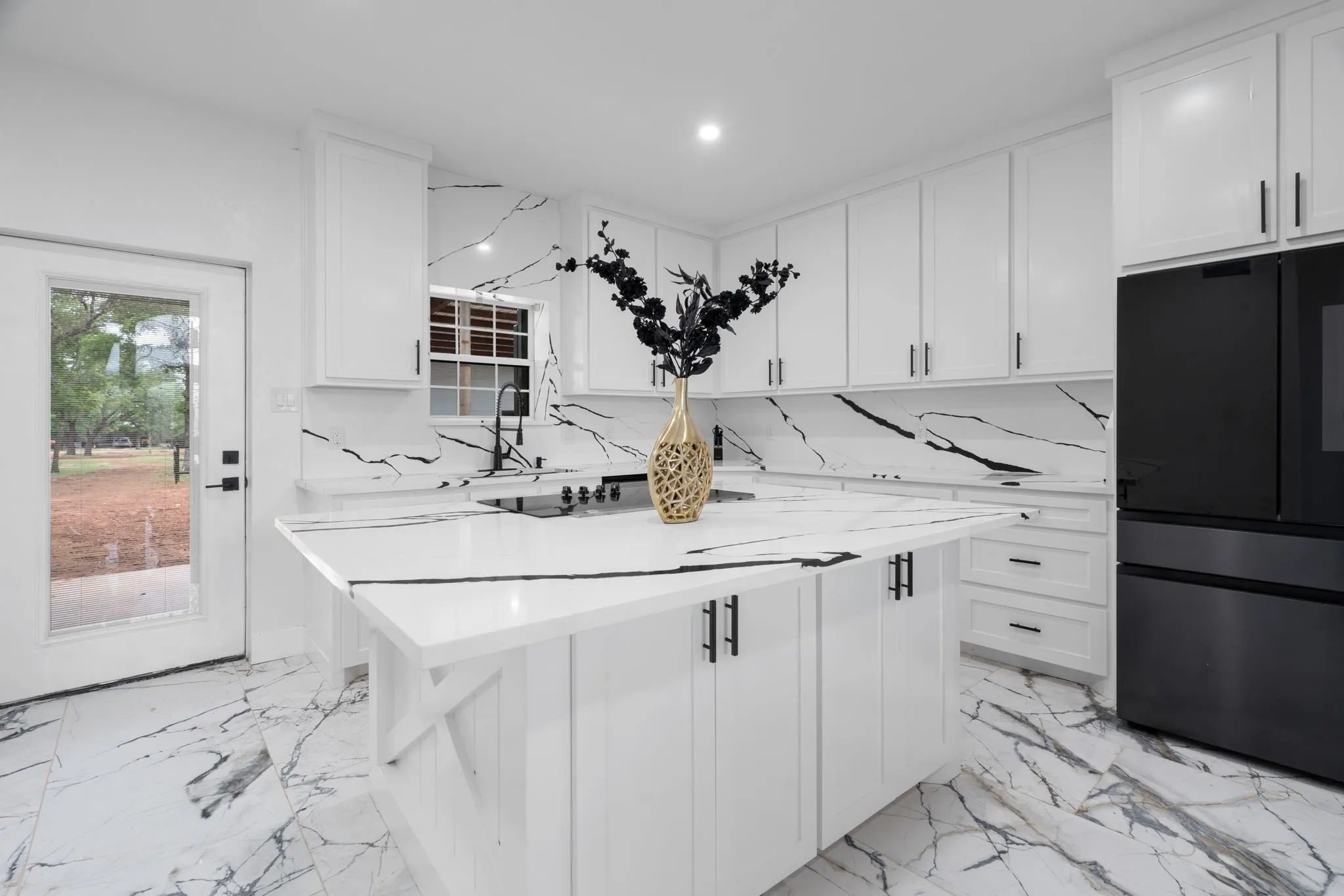 Modern kitchen featuring a white and black marbled countertop and backsplash, complemented by white cabinetry with black hardware
