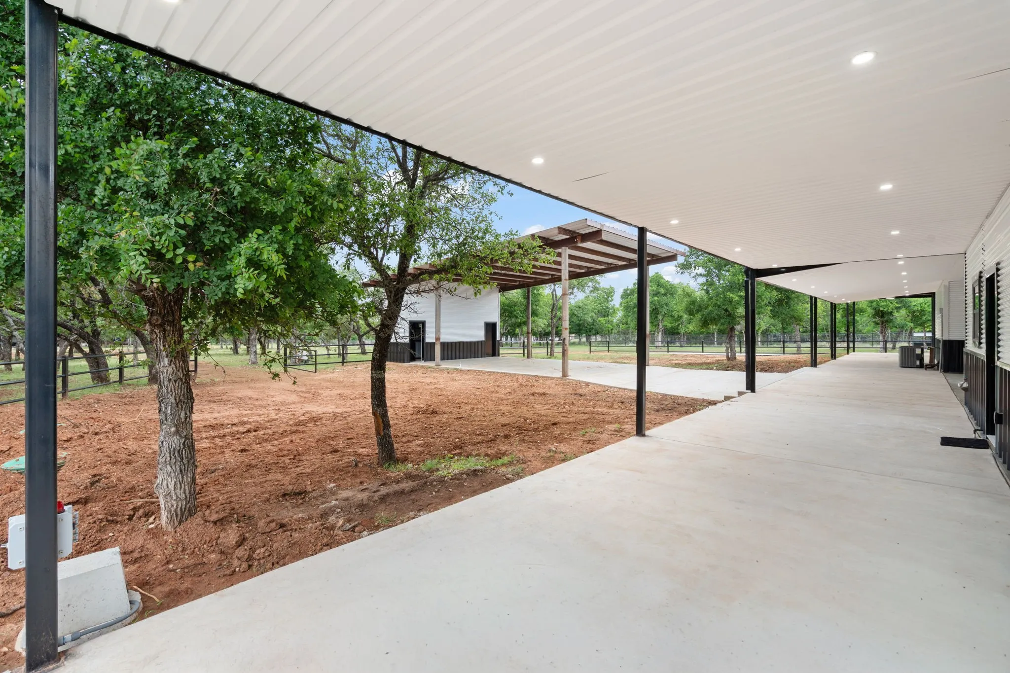 Expansive covered concrete walkway featuring recessed lighting, black structural columns, and a corrugated white ceiling