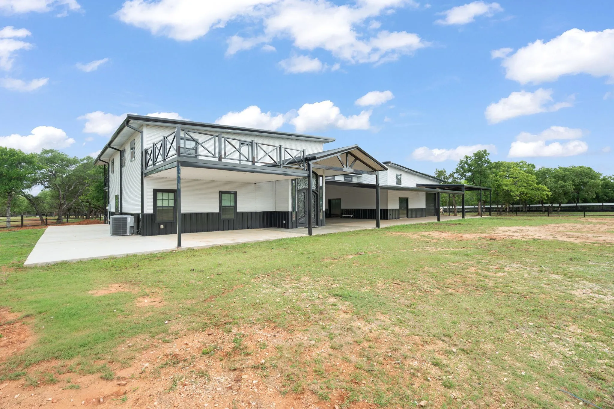 Two-story exterior with a covered patio, upper-level balcony featuring black railing, and an expansive concrete slab