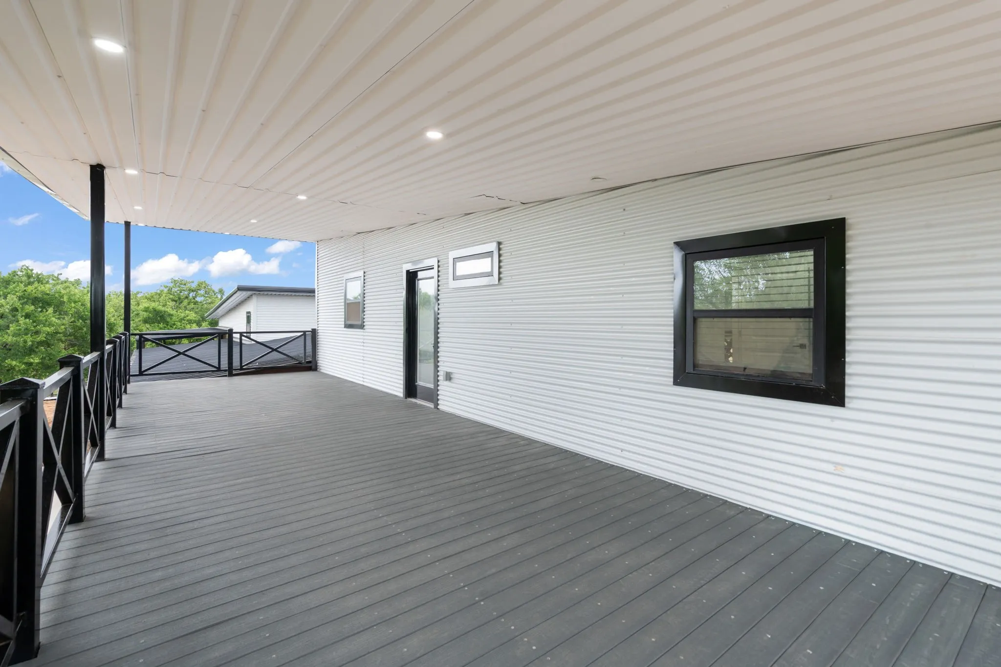 Expansive covered deck featuring composite wood-finish flooring, recessed lighting, and black metal railings
