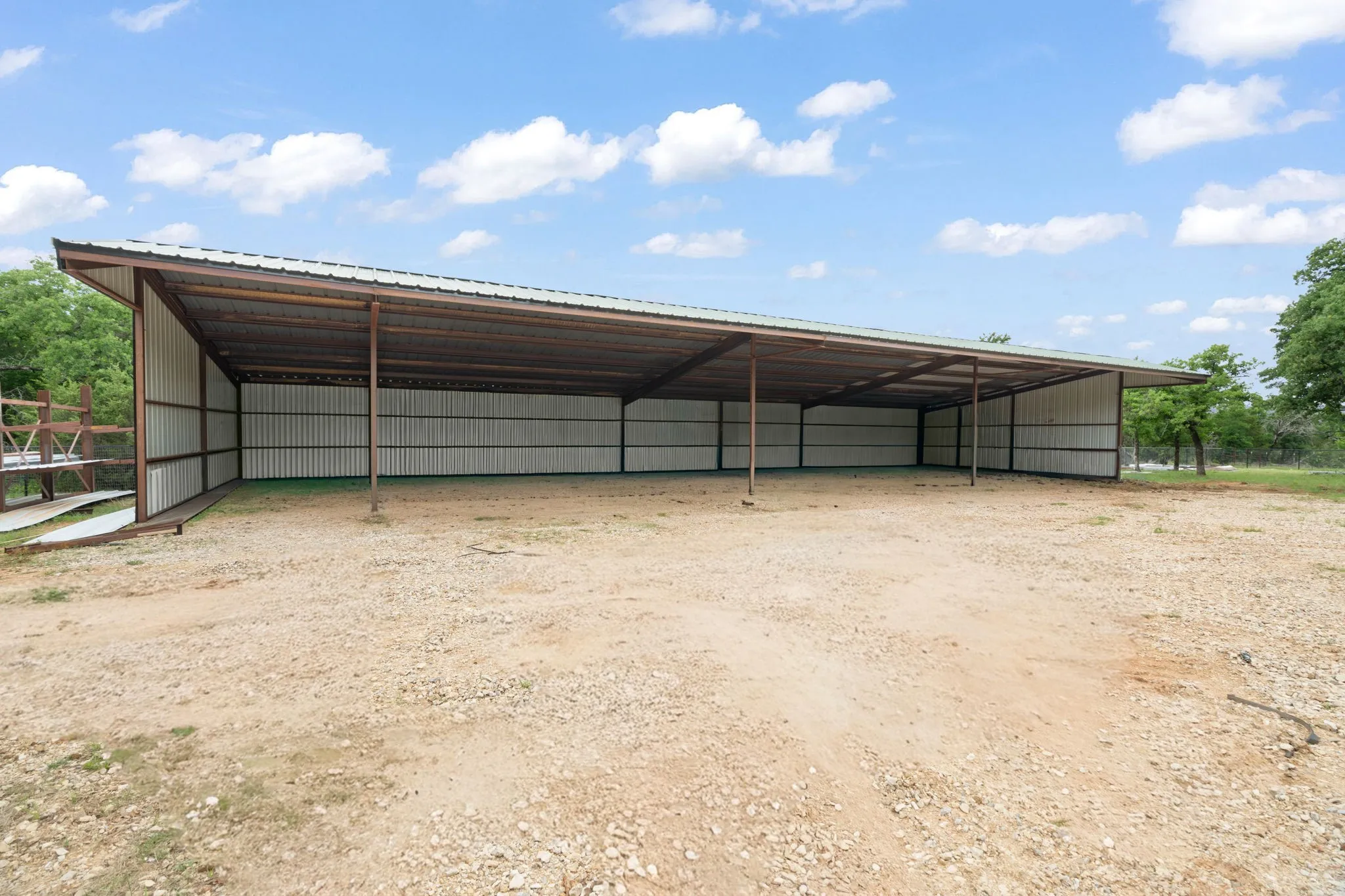 Open-sided metal structure featuring a pitched roof, metal siding, and a gravel-covered floor
