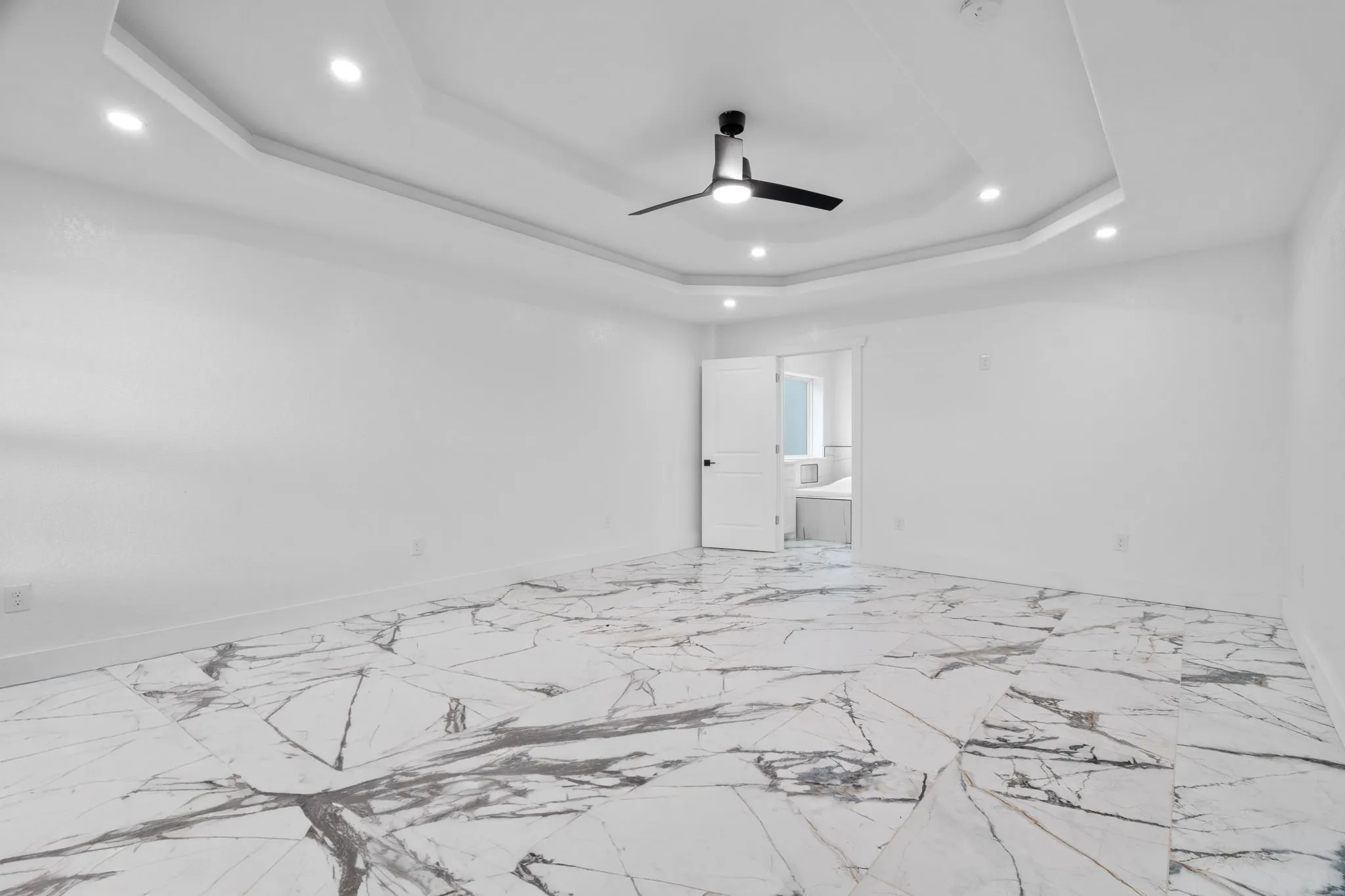 Spacious Primary bedroom featuring large-format tile flooring, a tray ceiling with recessed lighting, and a modern ceiling fan