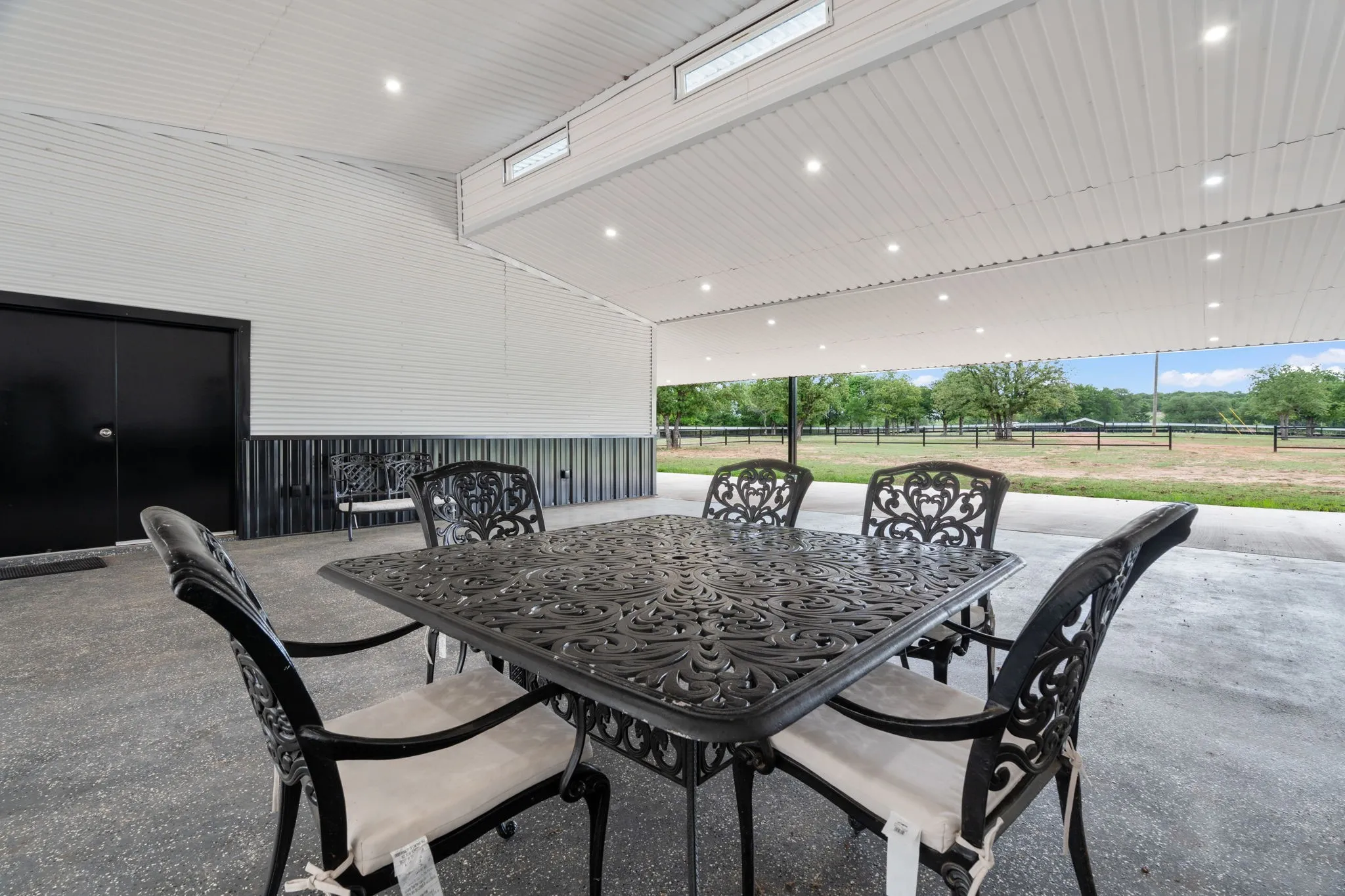 Covered outdoor patio with concrete flooring, recessed lighting, and a corrugated metal ceiling