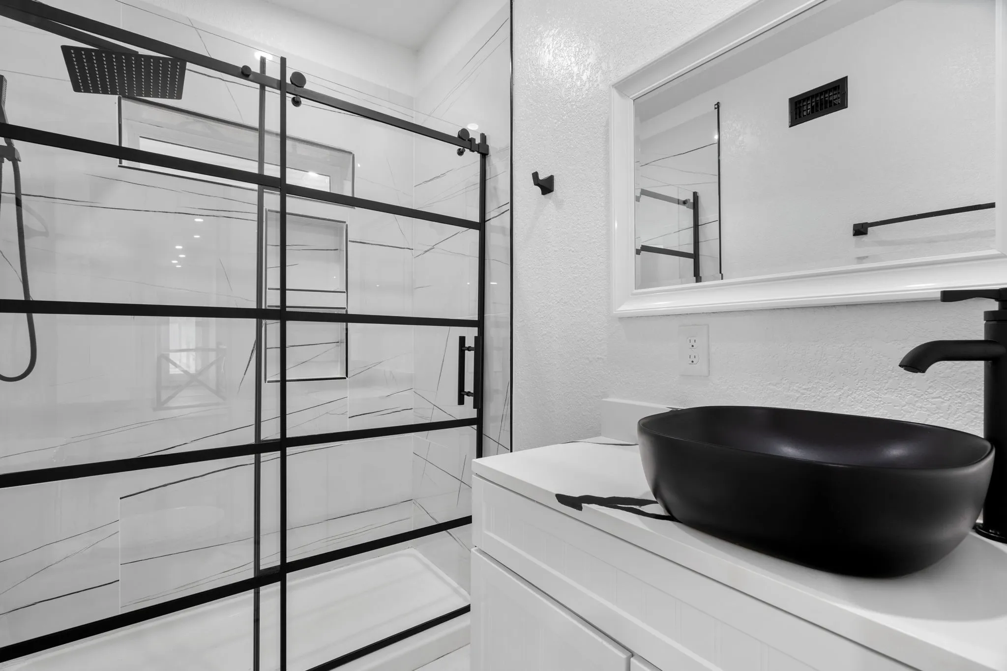 Modern bathroom Guest Quarters featuring a glass-enclosed shower with black grid accents, white marble-look wall tiling, a white vanity with a rectangular undermount sink, and a black faucet