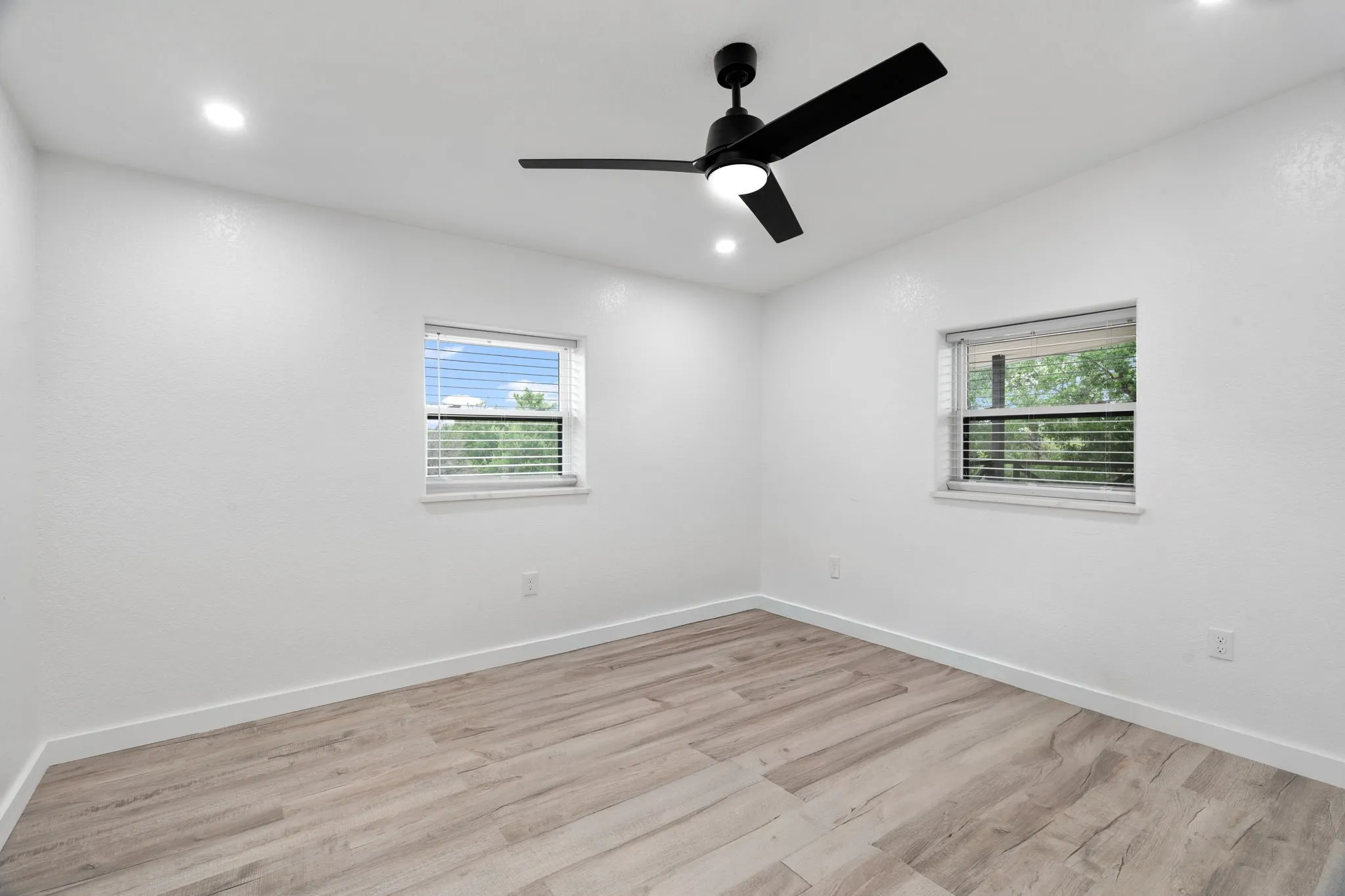 Guest quarters bedroom in shop Bright interior space featuring wood-finish flooring, two windows with blinds, a ceiling fan with integrated lighting, and recessed ceiling lights
