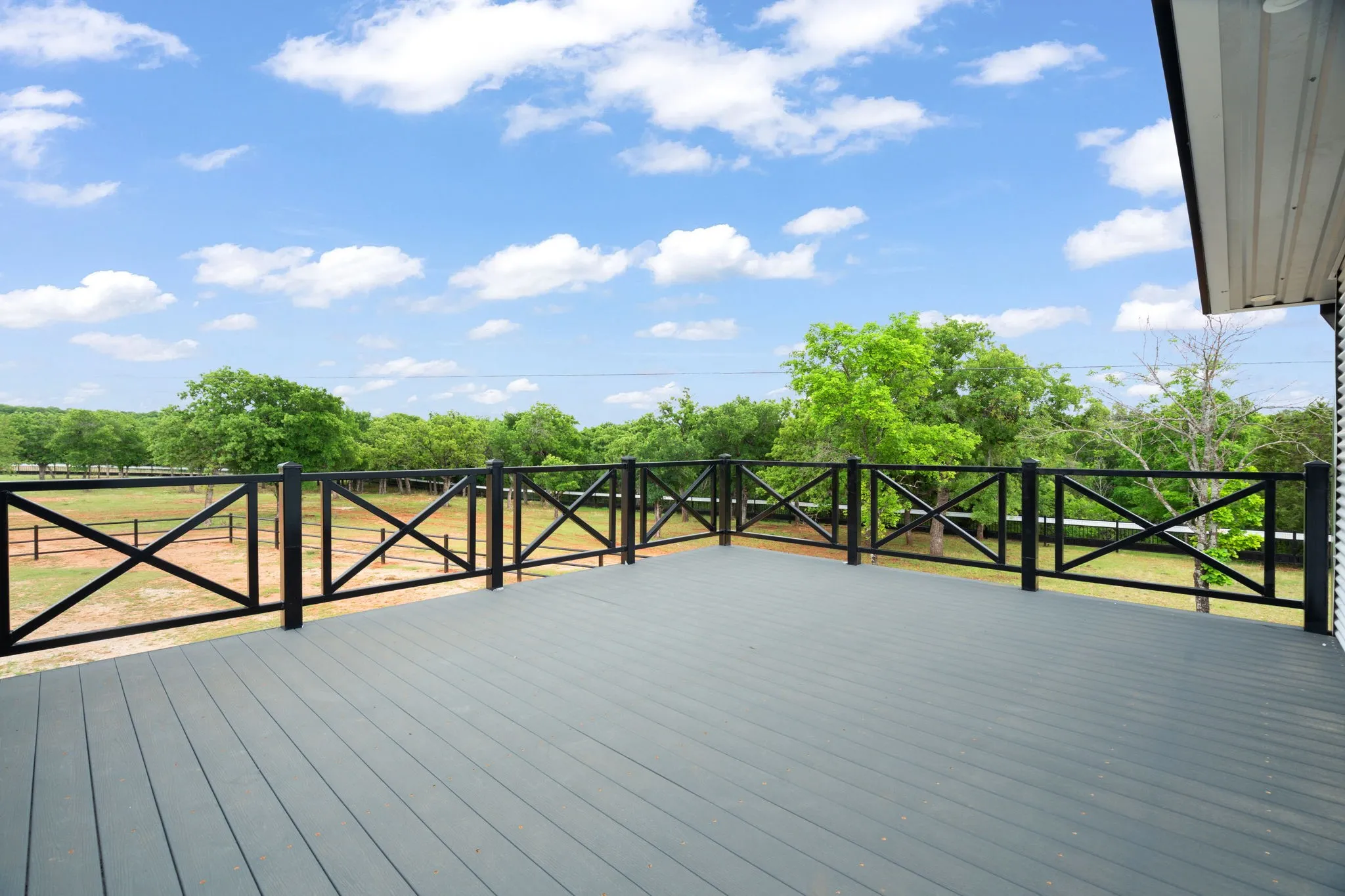 Spacious outdoor deck off front of home featuring composite wood-finish flooring, recessed lighting, and black metal railings