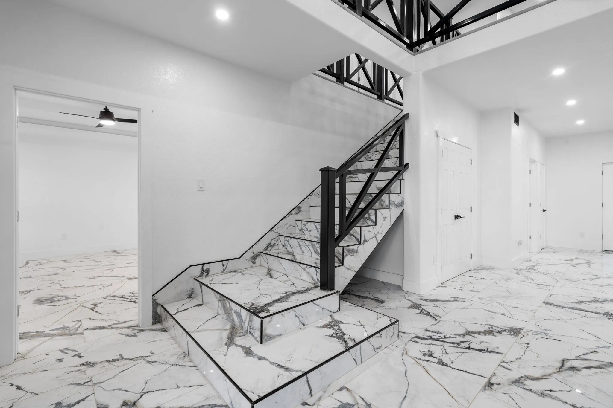 Grand staircase featuring marble-look risers and treads with a black trim and black metal railing