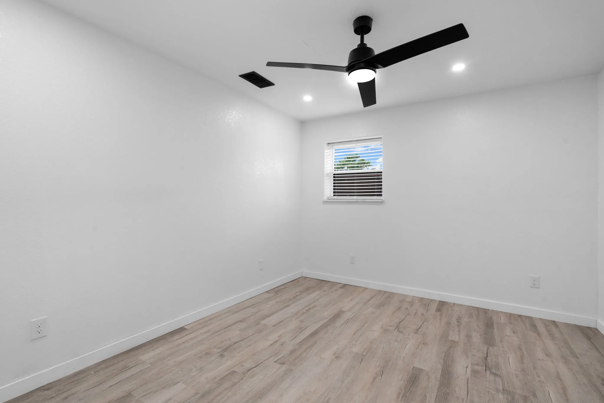 Guest bedroom featuring wood-finish flooring, a contemporary black ceiling fan with integrated lighting, recessed ceiling lights, and white baseboards