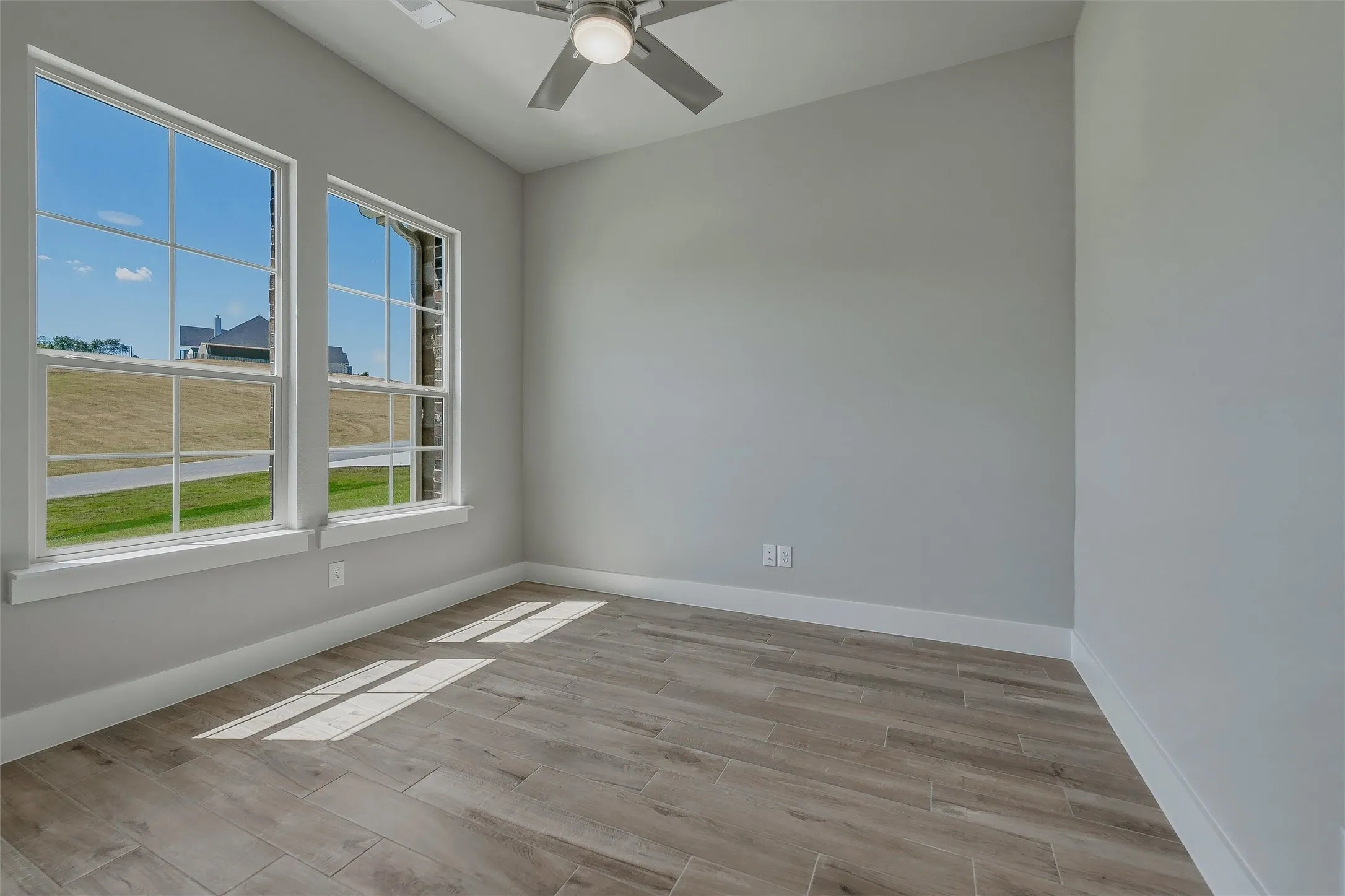 Vaulted ceiling, two large windows, wood-finish flooring, ceiling fan with light fixture, and light gray wall paint