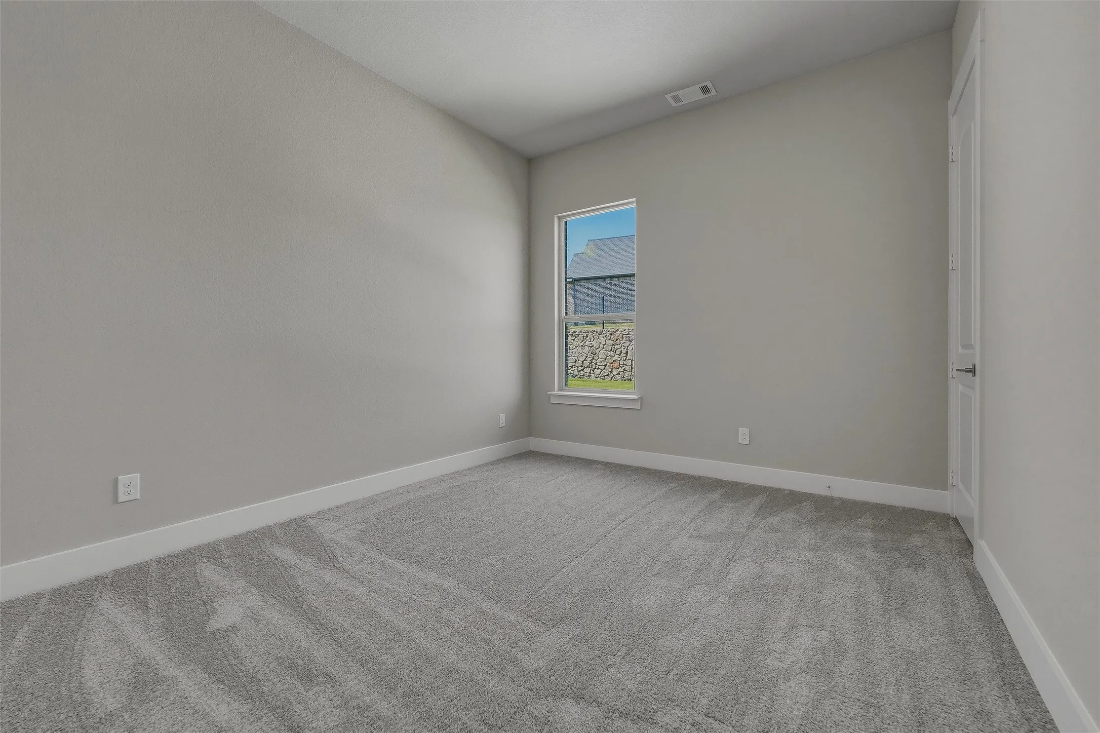 Sloped ceiling, neutral wall paint, light gray carpeting, white trim, and a window with exterior stone landscaping