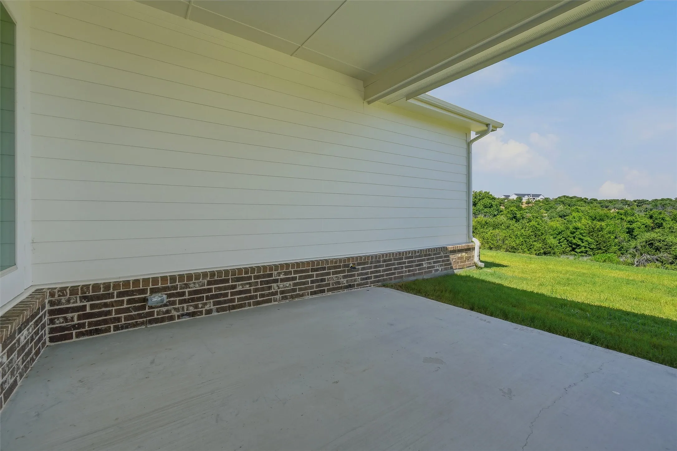 Covered patio with a concrete surface, brick foundation, and horizontal siding