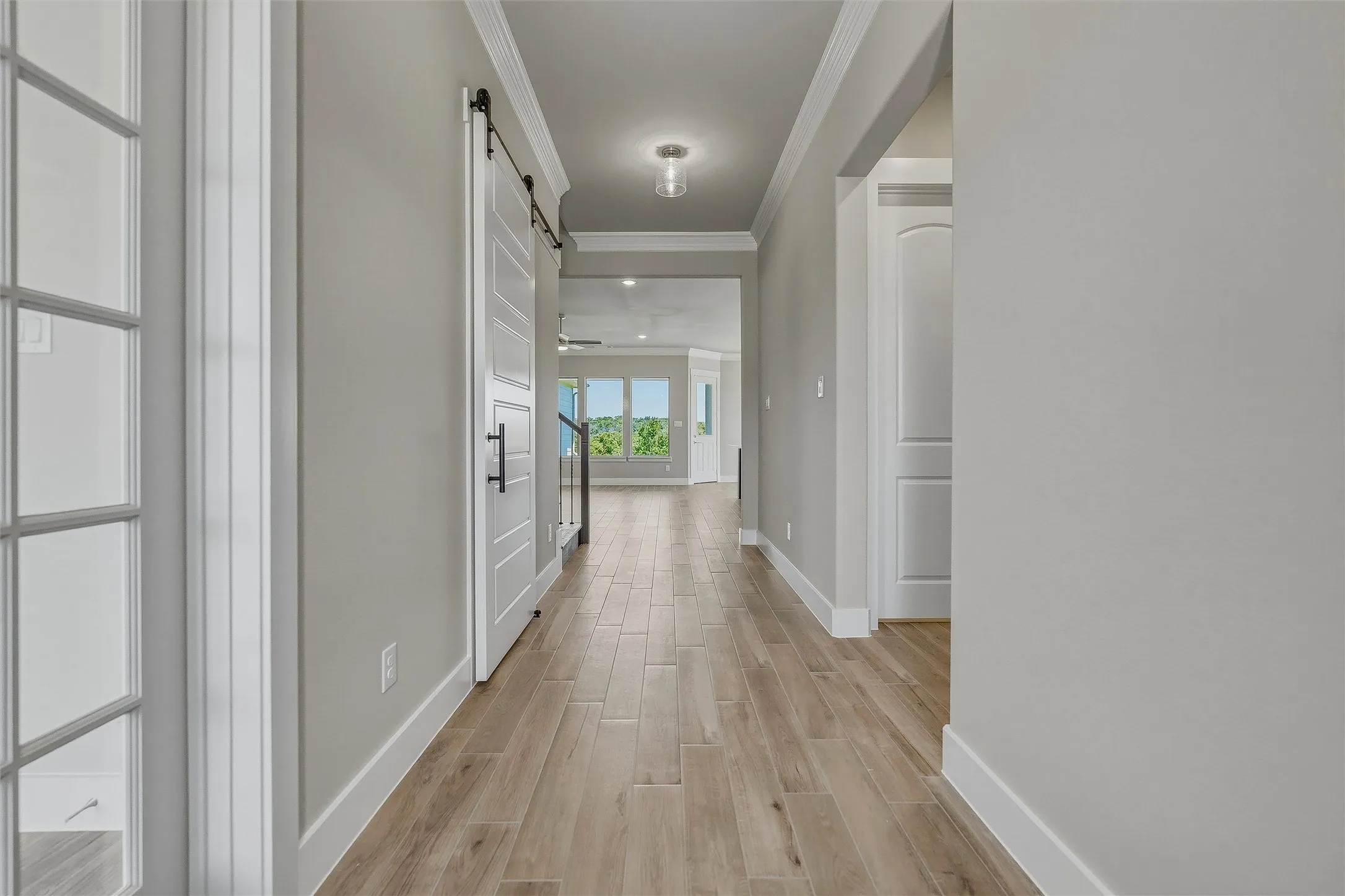 Wood-finish flooring, white paneled barn door, recessed lighting, white baseboards, and crown molding