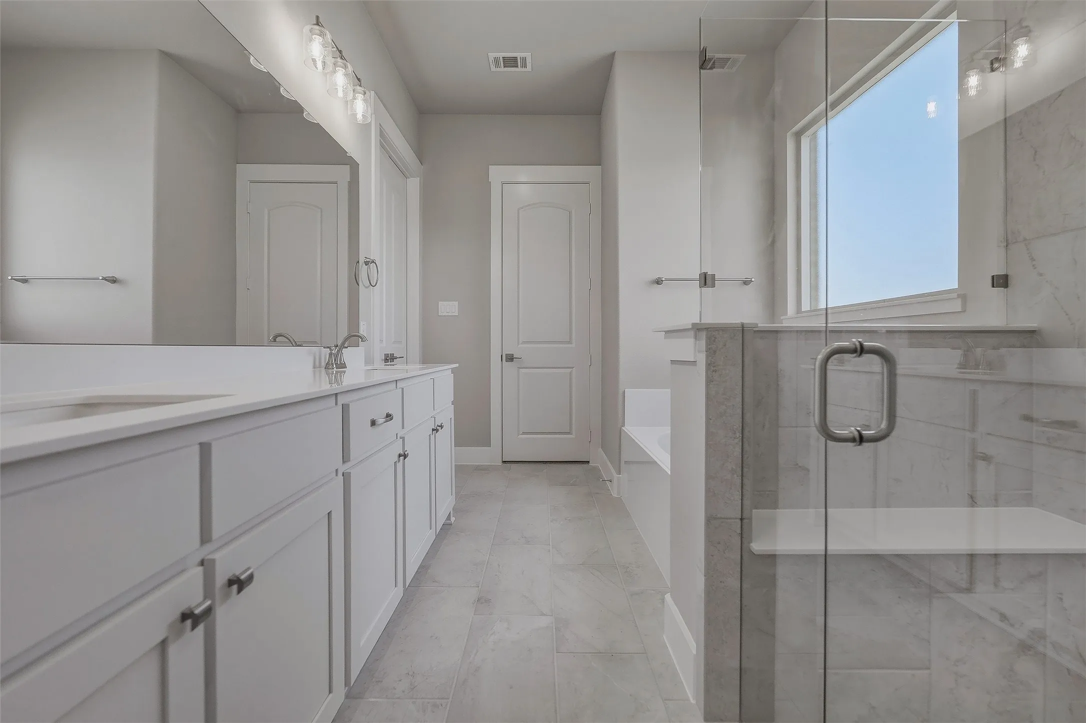 Dual vanity with white cabinetry and integrated sinks, a large frameless mirror, and a walk-in shower with clear glass enclosure and a built-in bench
