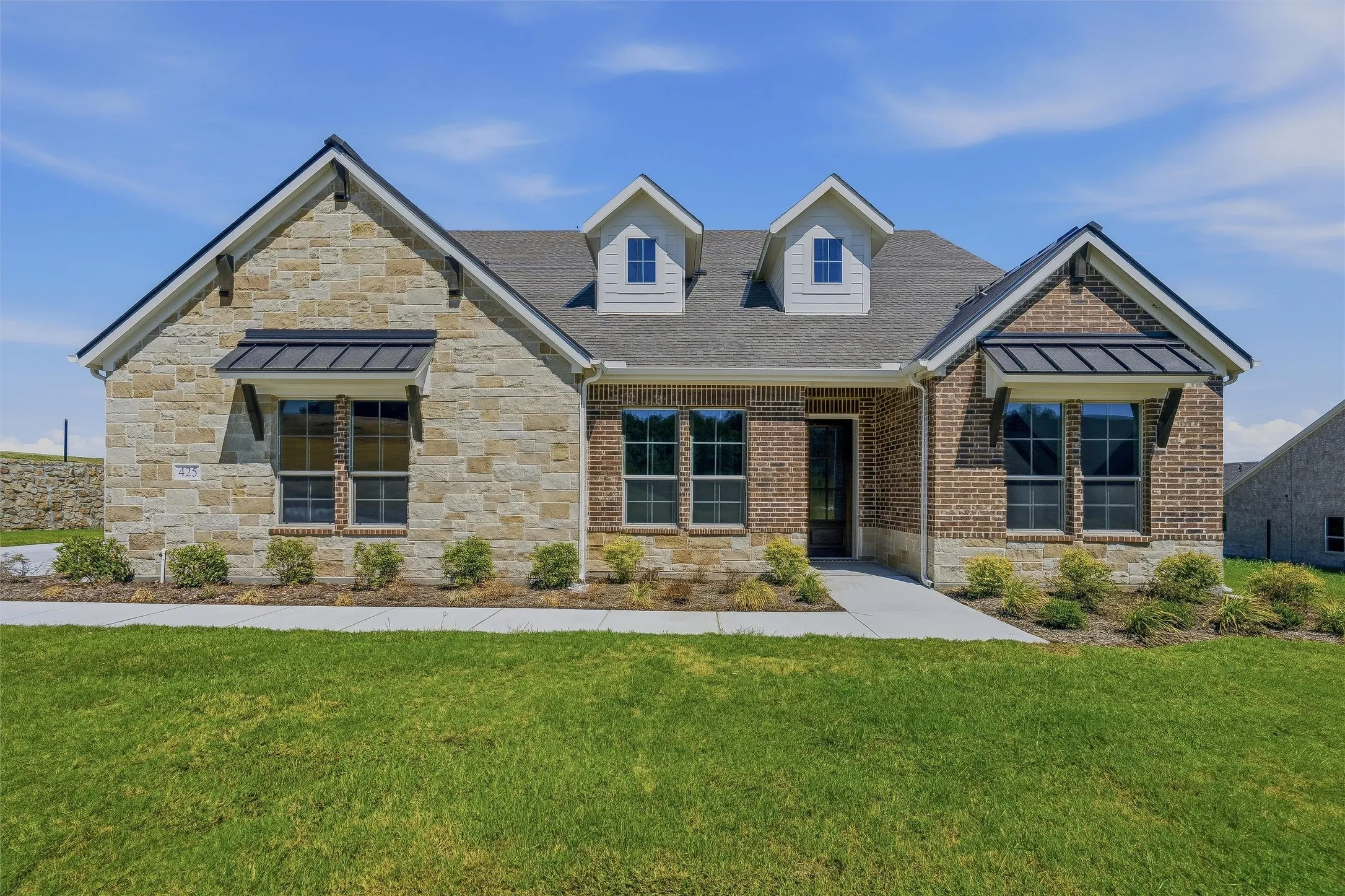 Stone and brick exterior with dormer windows, featuring black metal awnings and an attached two-car garage