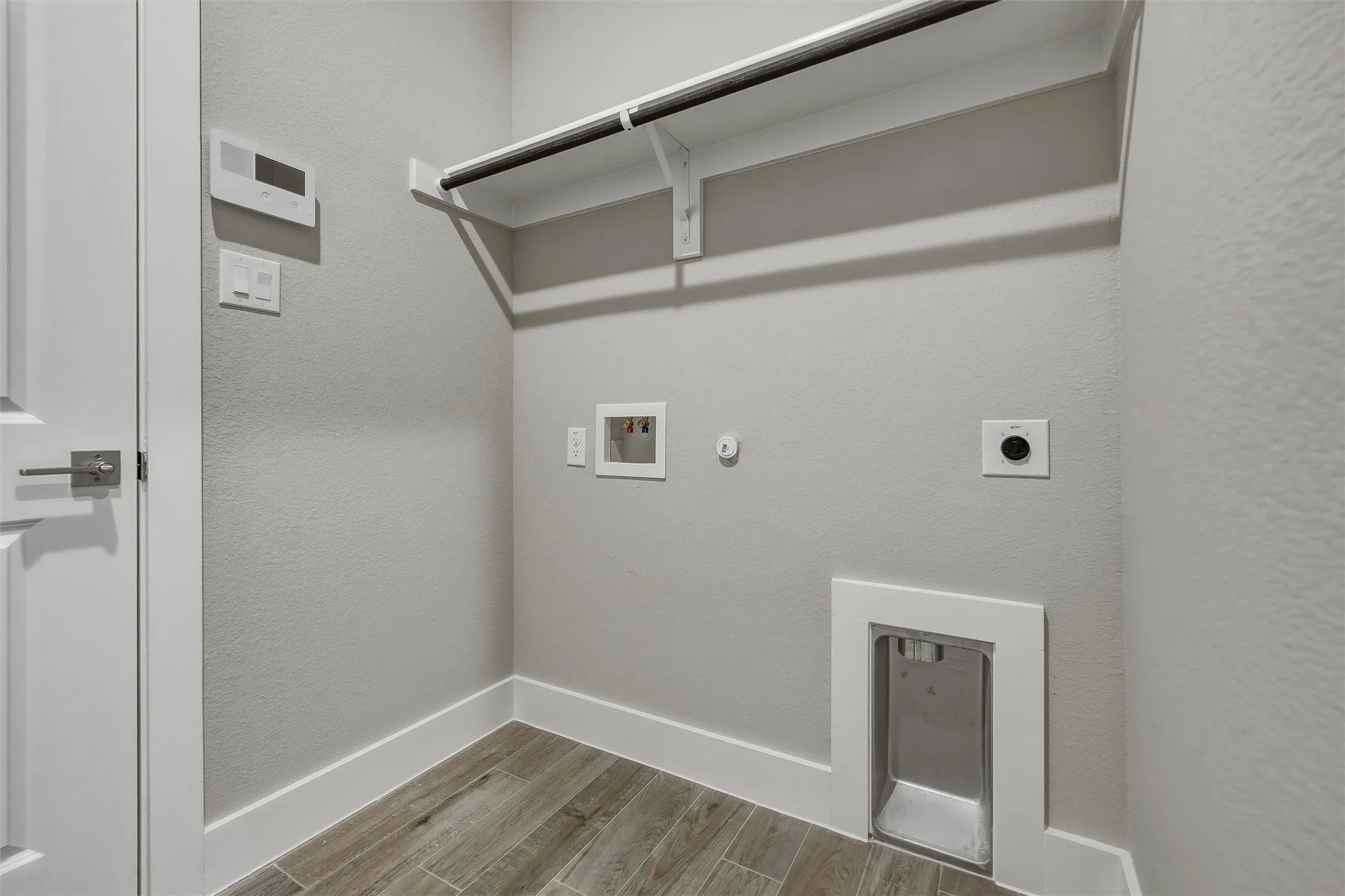 Utility space with wood-finish flooring, a wall-mounted shelving unit, and integrated appliance hookups