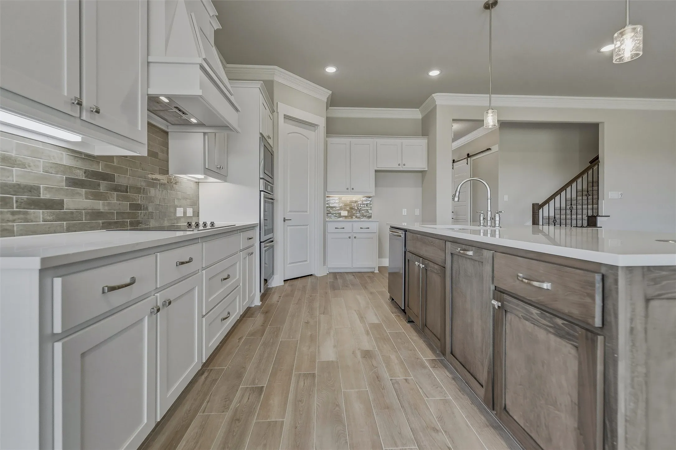 Kitchen featuring wood-finish flooring, white cabinetry, a stone backsplash, light-toned countertops, and a central island with an integrated sink
