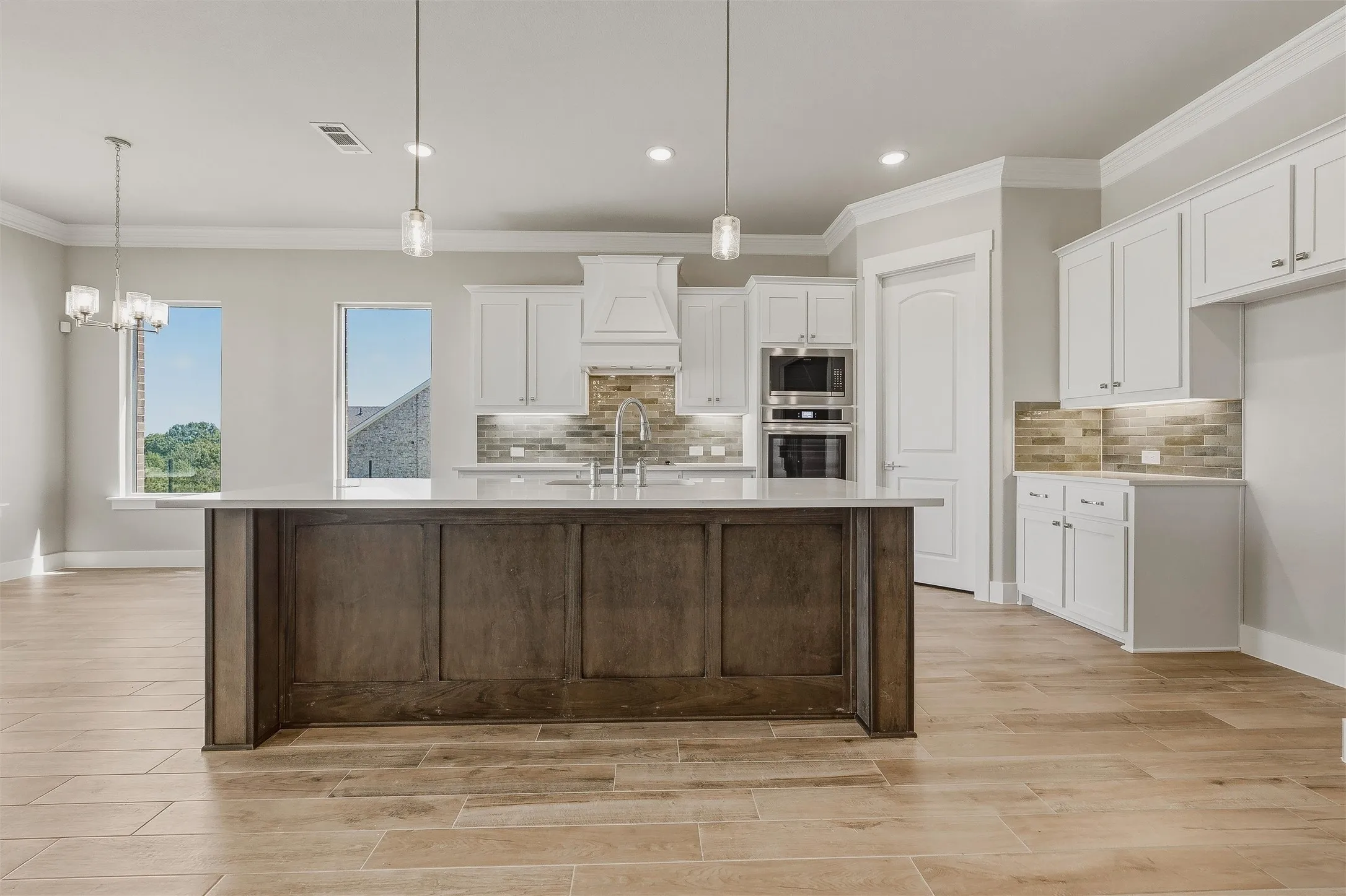 Kitchen with a large island featuring paneling, light wood-finish flooring, white cabinetry, integrated stainless steel appliances, and a tiled backsplash